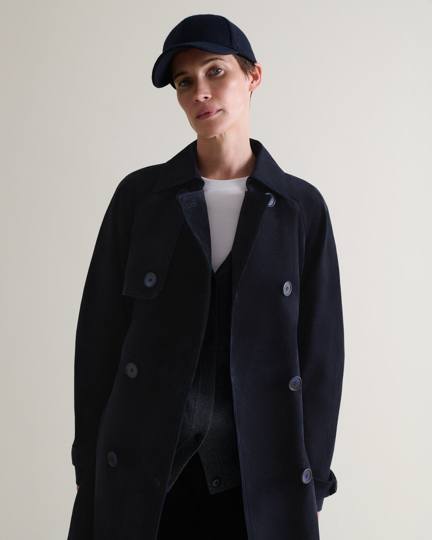 Front view of woman wearing navy cashmere merino wool baseball cap with matching suede trench coat and a white t-shirt.