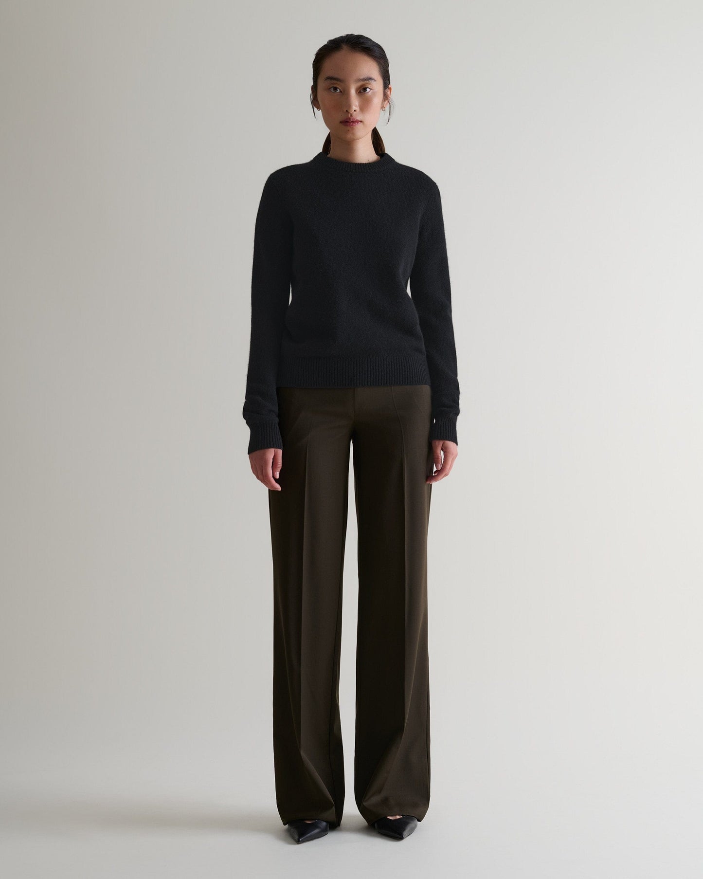 Image 1 of 4 showing woman wearing Rise & Fall's black mid-weight cashmere crew neck jumper with brown silk trousers.