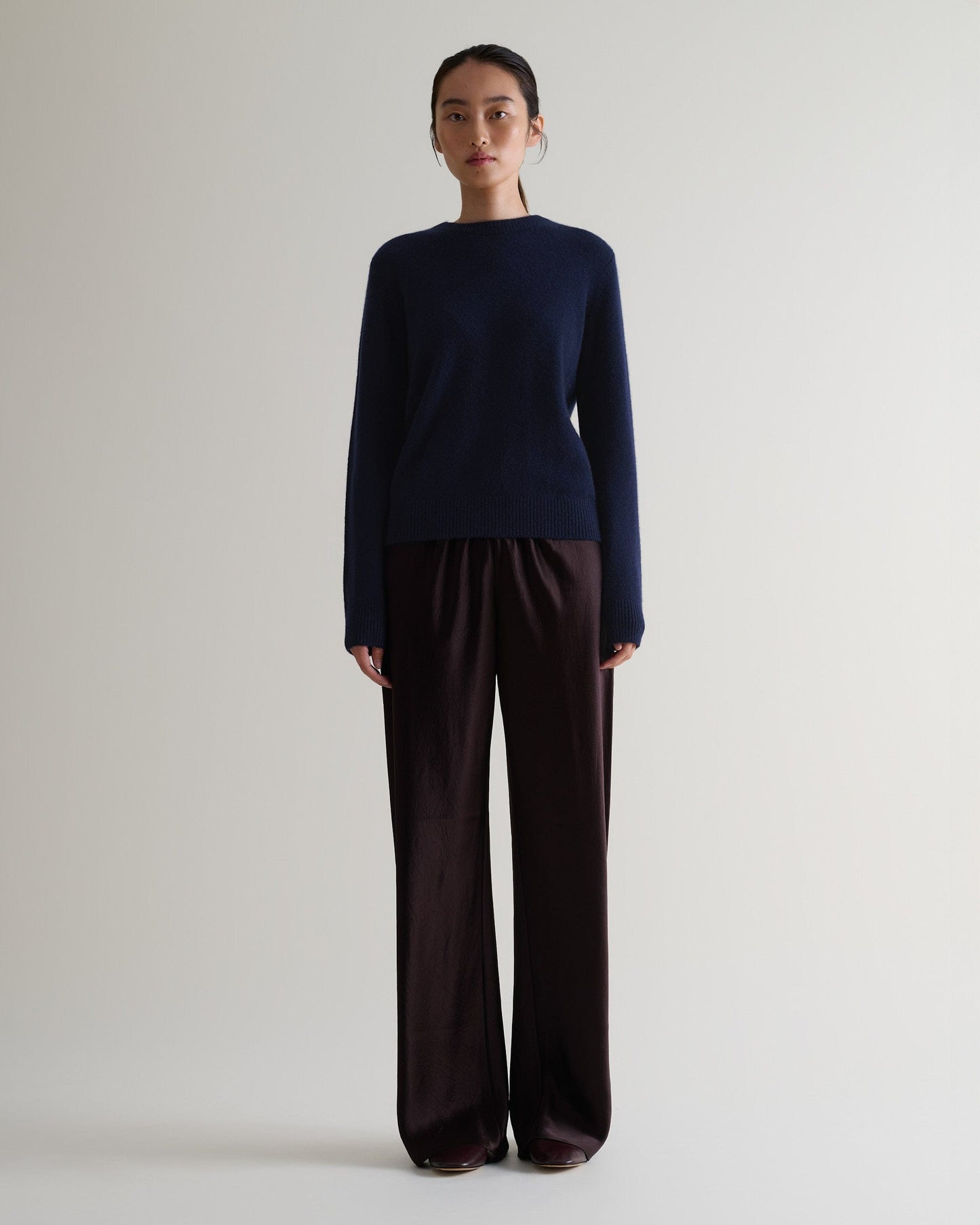 Image 1 of 5 showing woman wearing Rise & Fall's navy mid weight cashmere crew neck jumper with brown silk trousers.