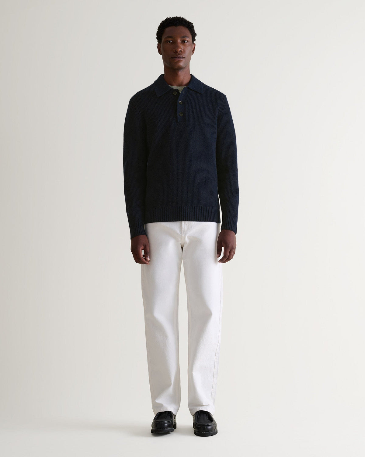 Image 1 of 6 showing man wearing Rise & Fall's navy cashmere merino fisherman ribbed polo sweater with white jeans and black shoes.