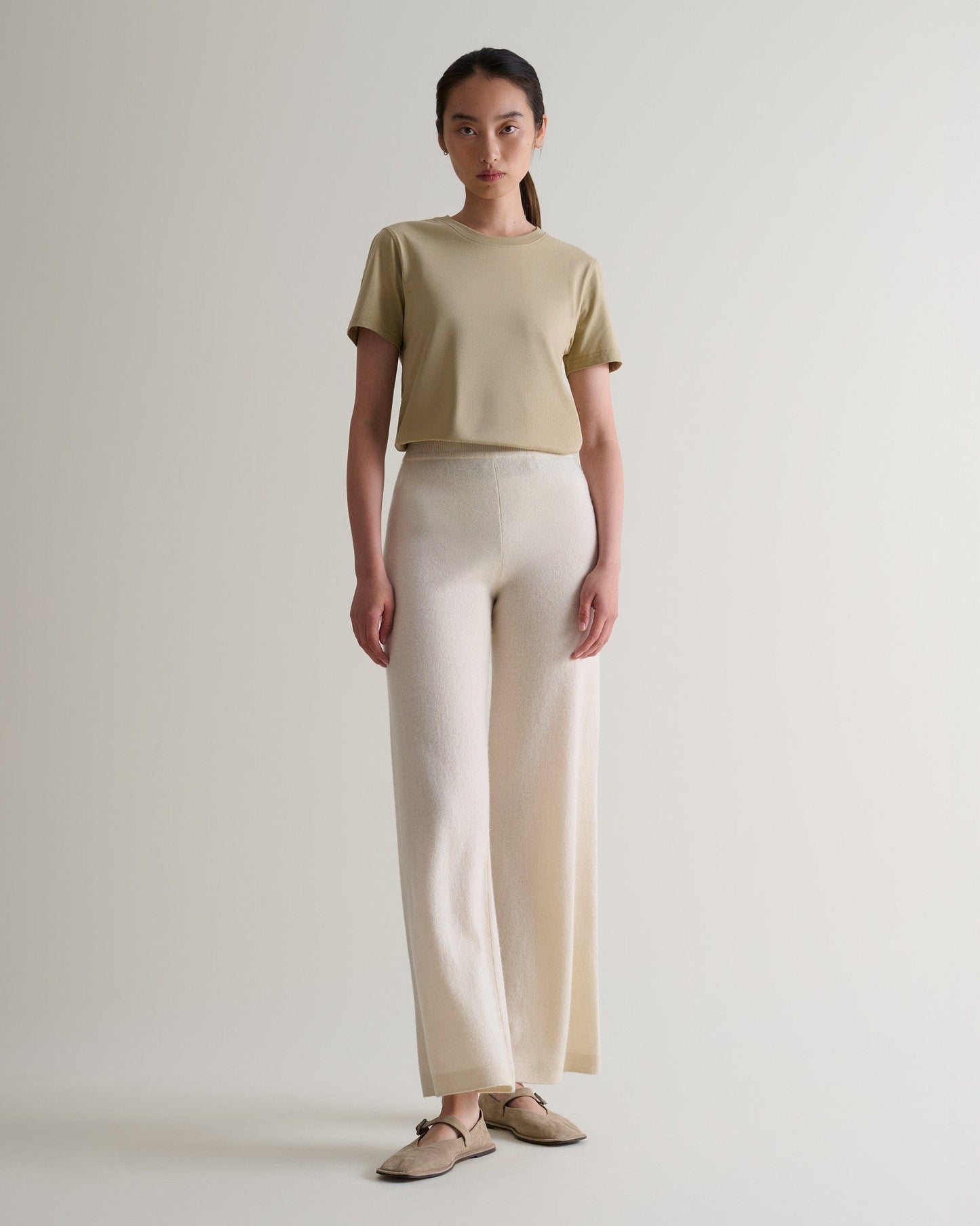 Image 1 of 6 showing woman wearing Rise & Fall's cream fine cashmere wide-leg trousers with beige t-shirt and shoes.