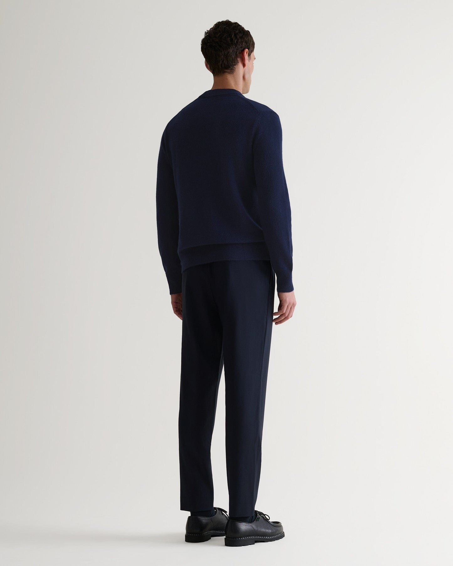 Image 3 of 4 showing back of man wearing Rise & Fall's Finest Cashmere Mid-Weight Crew Neck Jumper in navy with tailored black trousers.
