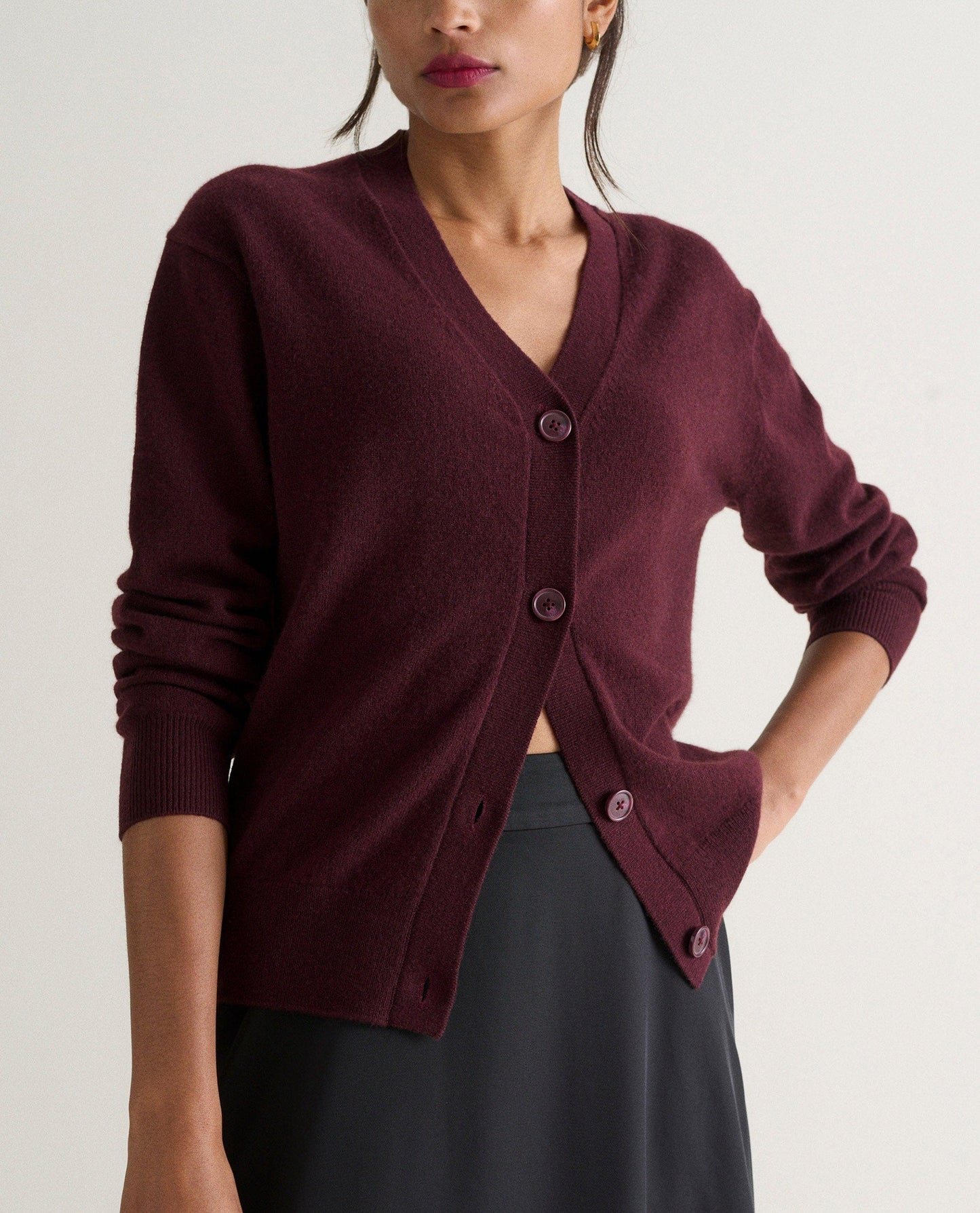 Image 3 of 4 showing woman wearing Rise & Fall's oxblood fine cashmere v-neck cardigan with black skirt.