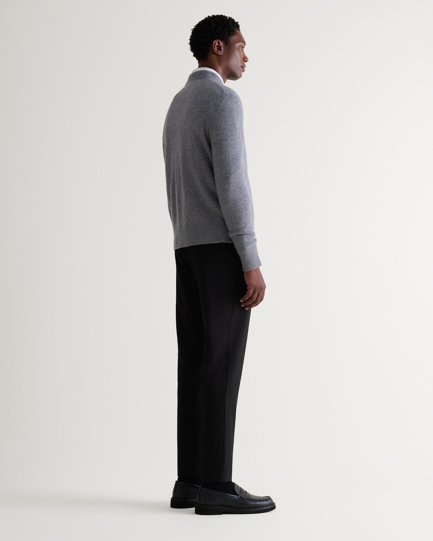 Image 3 of 5 showing side view of man wearing Rise & Fall's finest cashmere mid-weight crew neck jumper in grey with white shirt and black jeans.