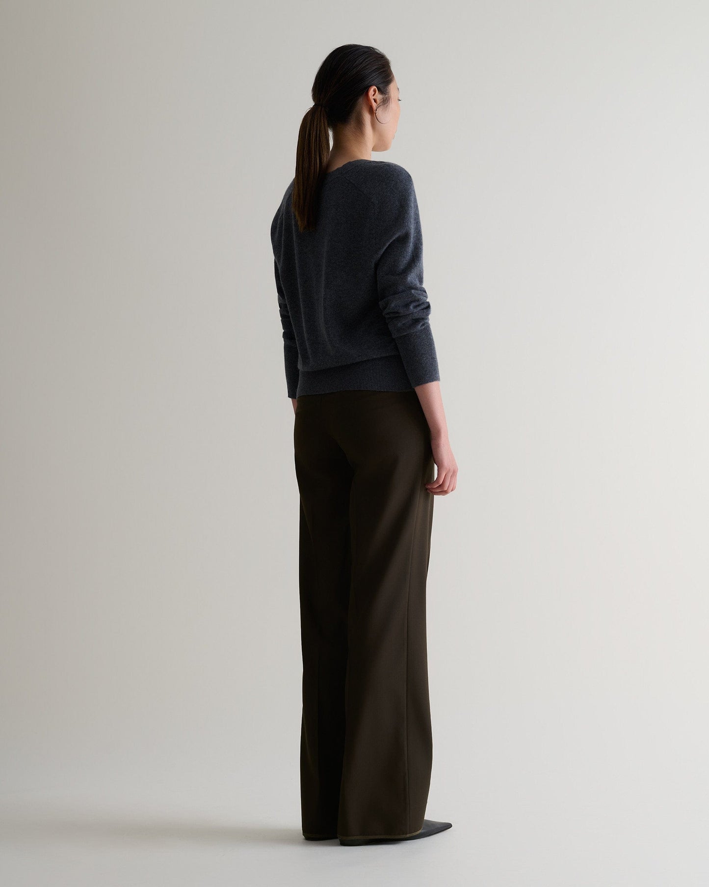 Image 3 of 5 showing back of woman wearing Rise & Fall's fine cashmere blouson cardigan, colour: graphite.