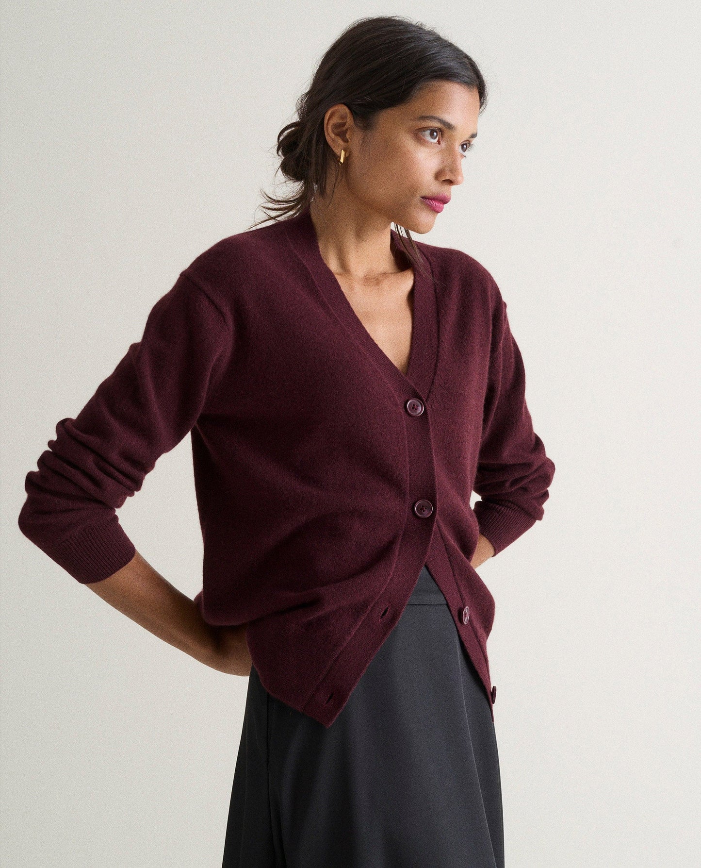 Image 4 of 4 showing side view of woman wearing Rise & Fall's oxblood fine cashmere v-neck cardigan with black skirt.