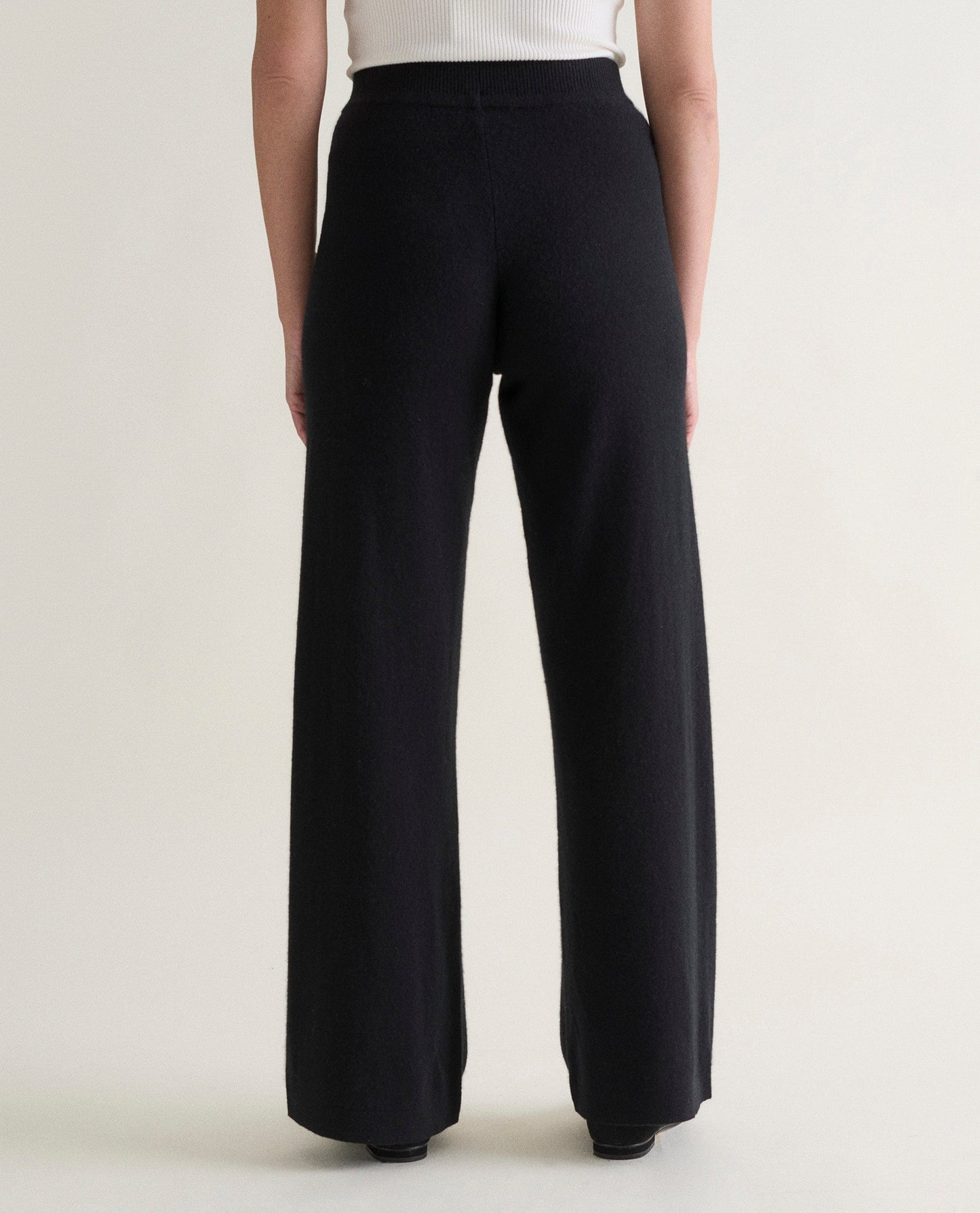 Image 4 of 4 showing back of woman wearing Rise & Fall's black fine cashmere wide-leg trousers with a white top.
