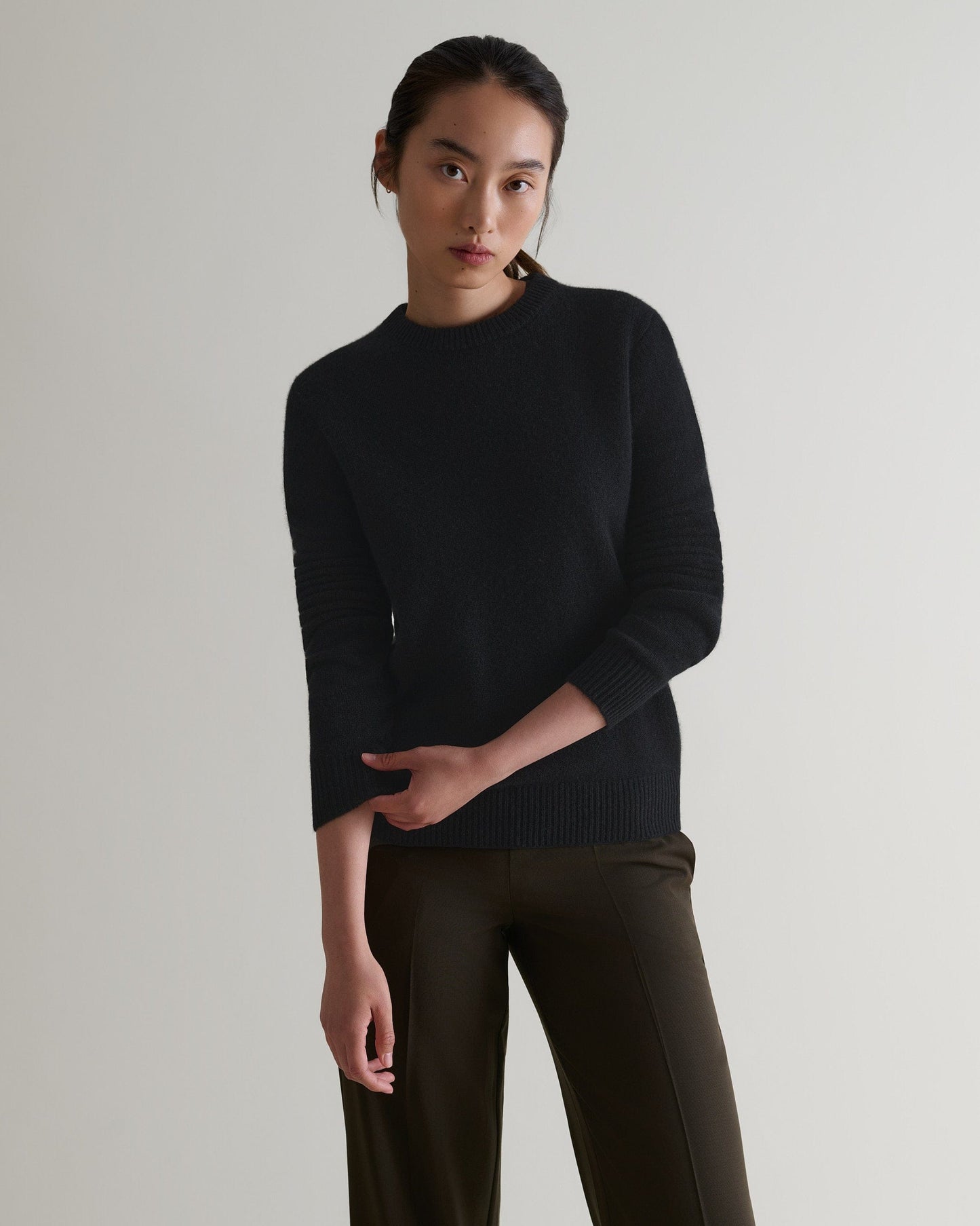 Image 4 of 4 showing woman wearing Rise & Fall's black mid-weight cashmere crew neck jumper with brown silk trousers.