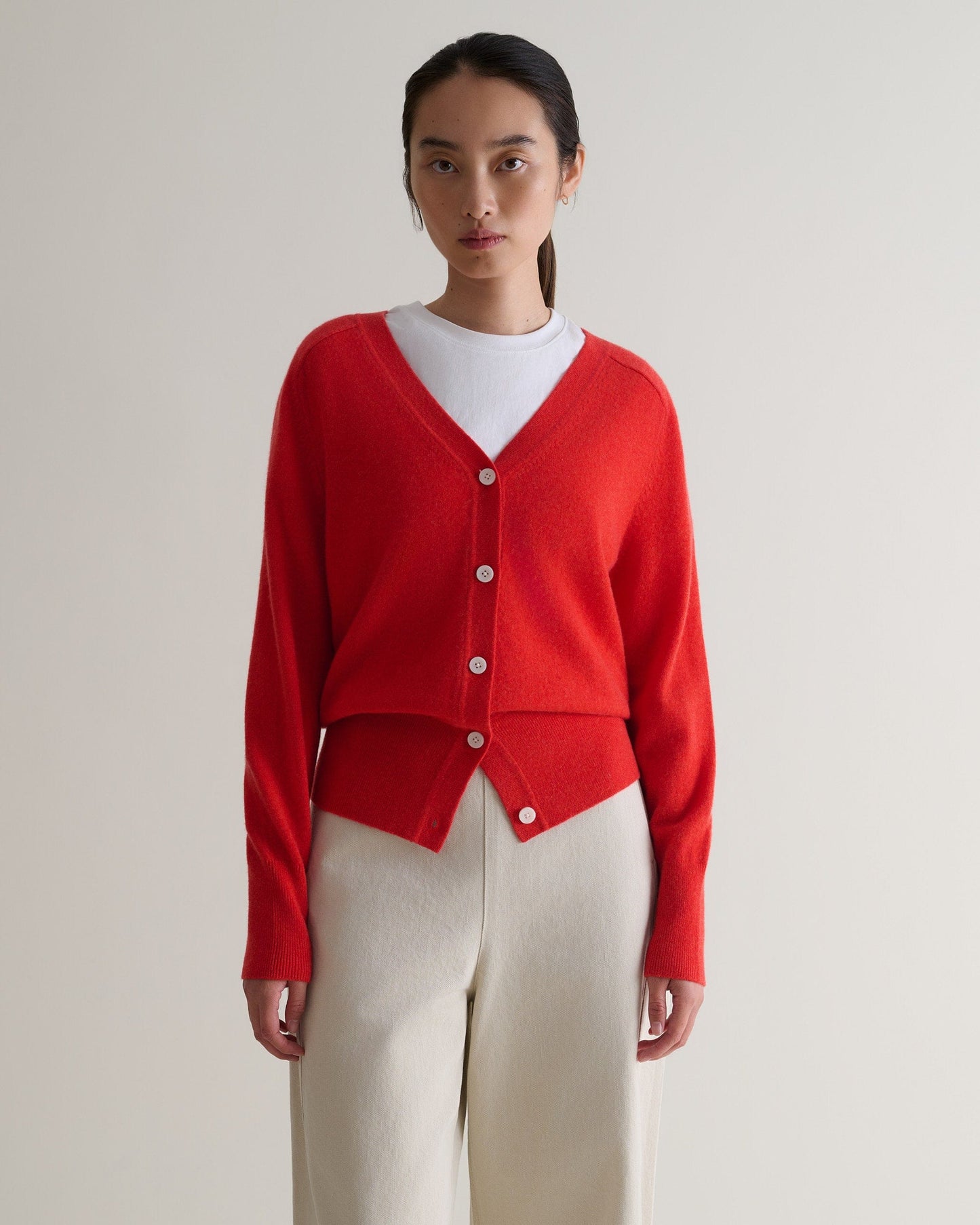 Image 4 of 5 showing woman wearing Rise & Fall's poppy red fine cashmere blouson cardigan with white T-shirt and cream trousers.
