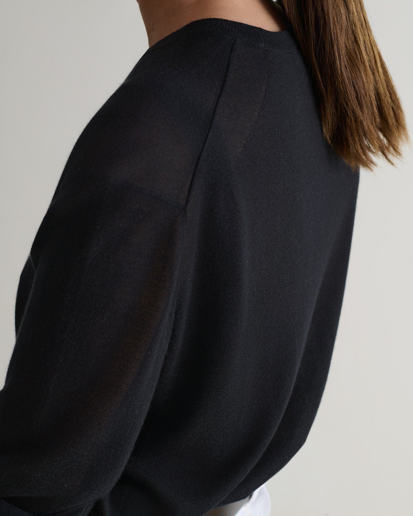 Image 4 of 5 showing a close up side view of a woman wearing Rise & Fall's black tencel cashmere double layered crew neck jumper.