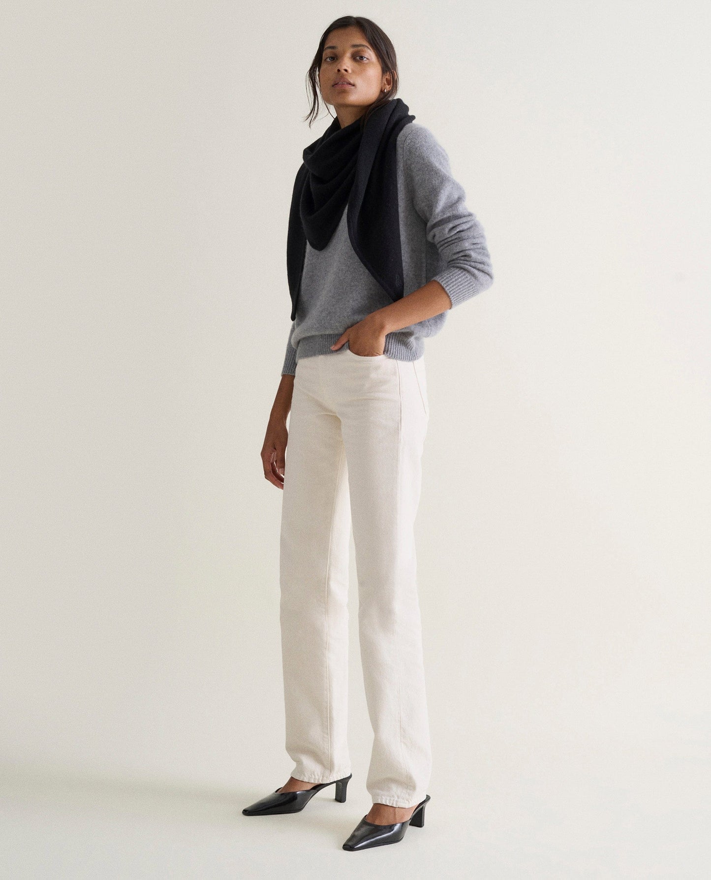 Image 4 of 5 showing woman wearing Rise & Fall's grey mid-weight cashmere crew neck jumper with white jeans and navy cashmere scarf.