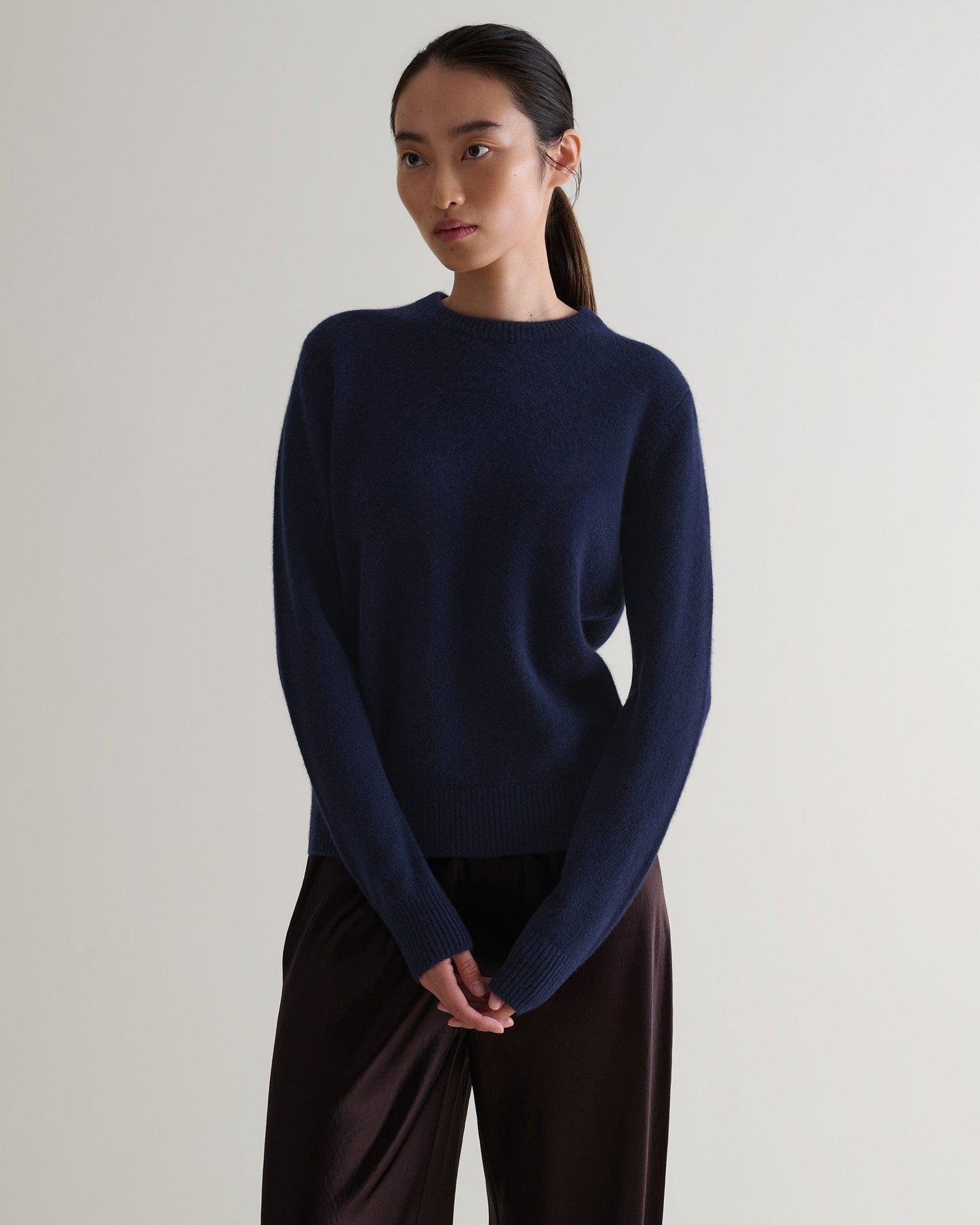 Image 4 of 5 showing woman wearing Rise & Fall's navy mid weight cashmere crew neck jumper with brown silk trousers.
