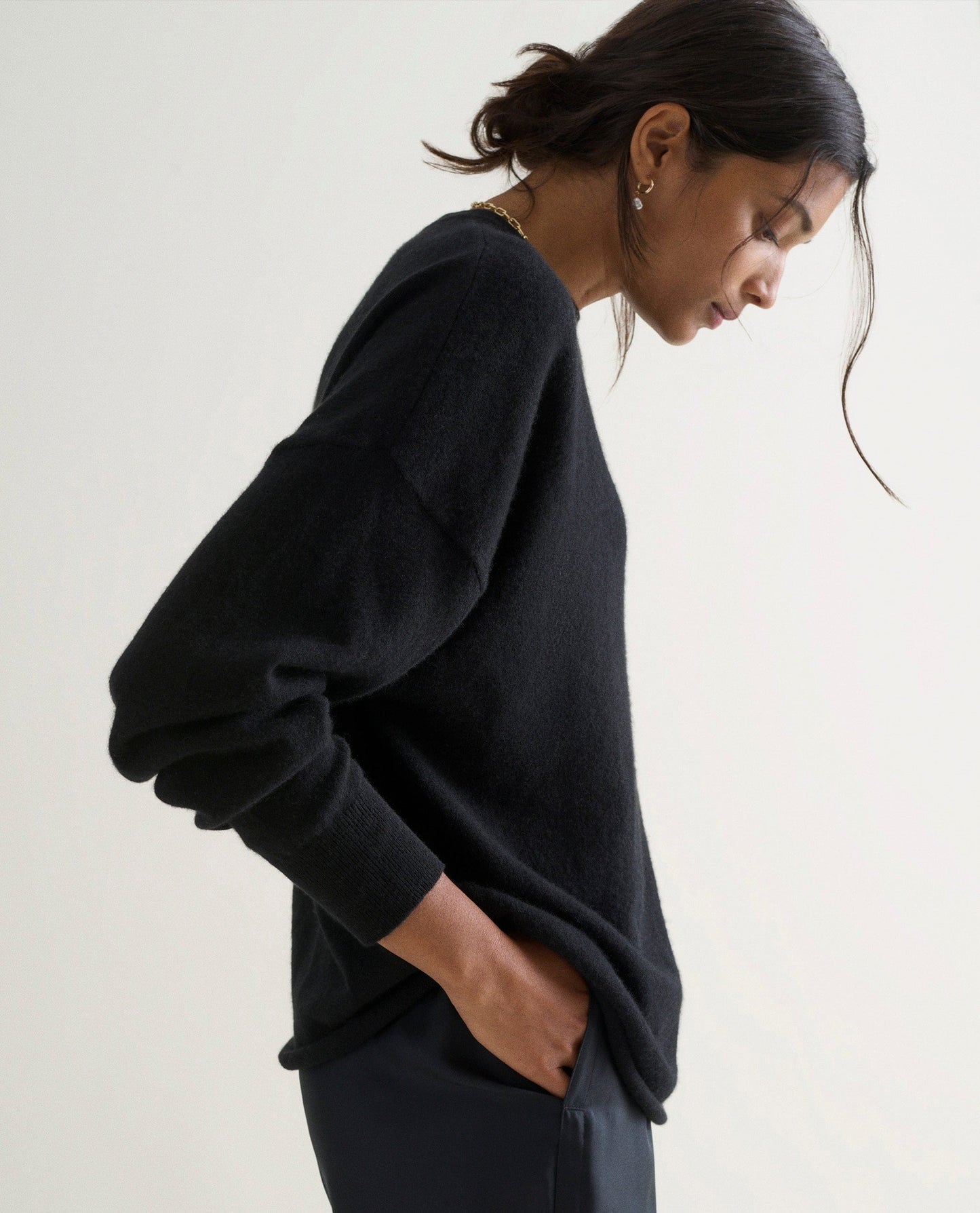 Image 4 of 6 showing the side of a woman wearing Rise & Fall's black fine cashmere sweatshirt with black silk trousers.