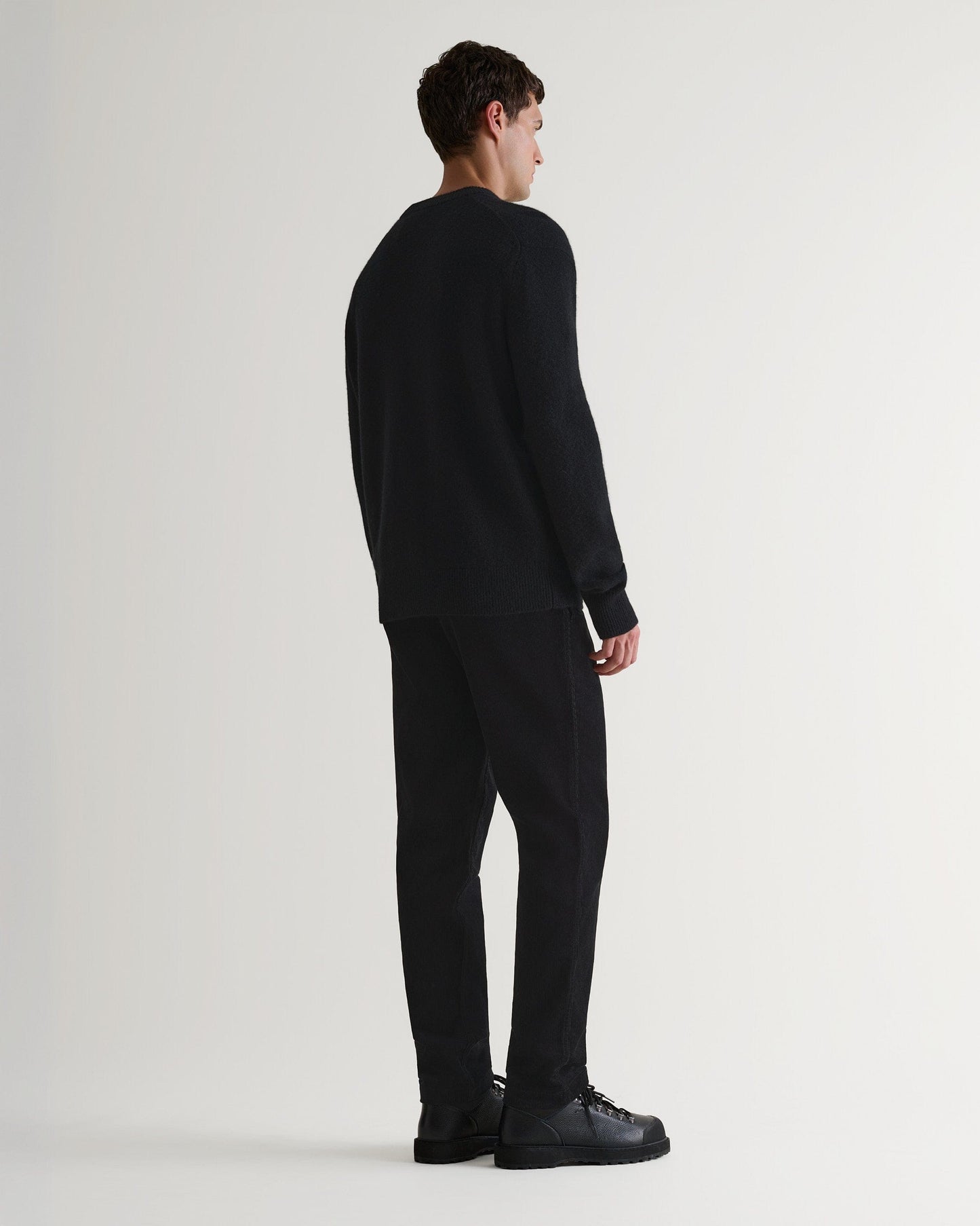 Image 4 of 7 showing back of man wearing Rise & Fall's Finest Cashmere Mid-Weight Crew Neck Jumper in black with tailored black trousers.