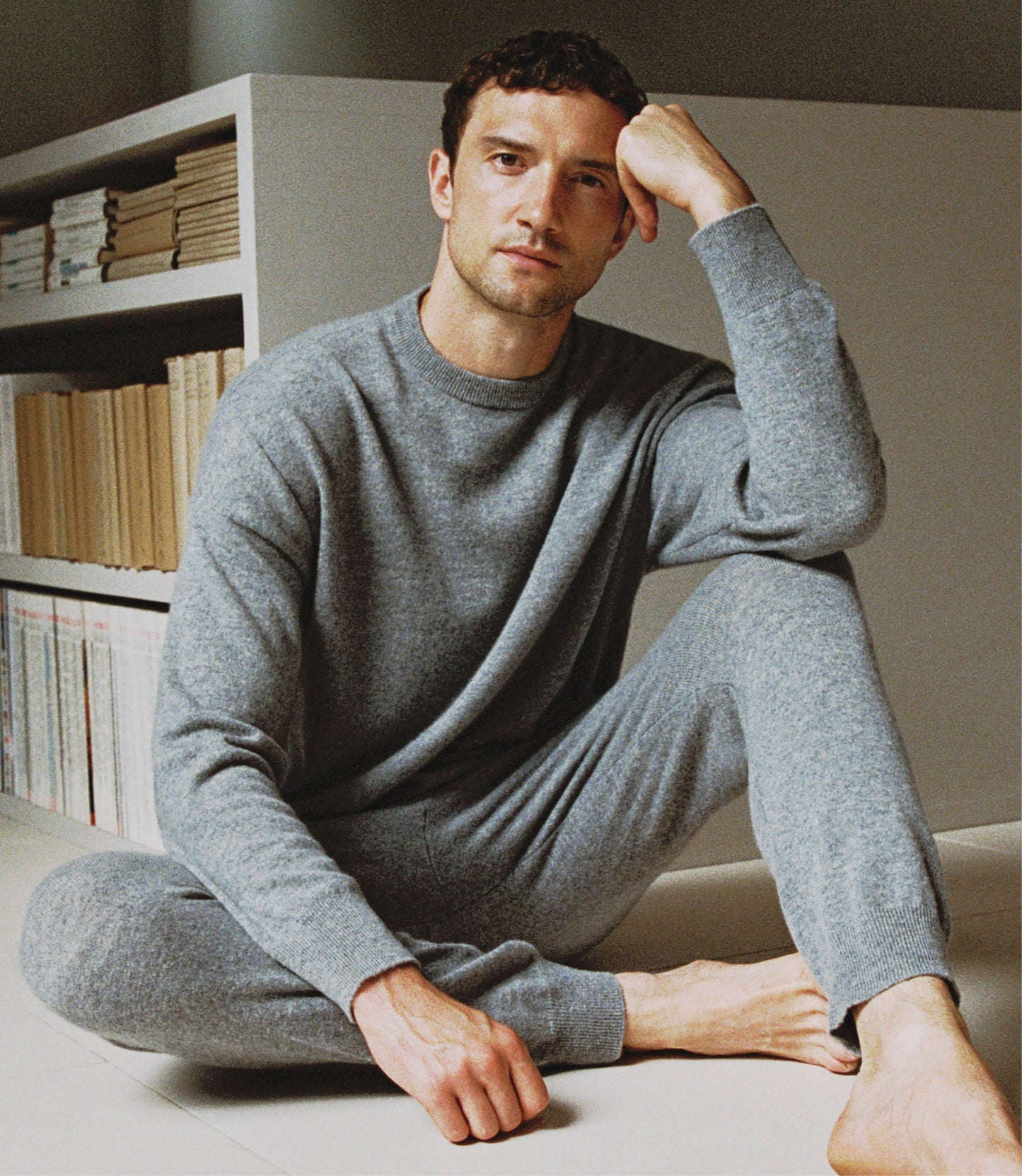 Image 5 of 5 showing man sat on floor wearing Rise & Fall's finest cashmere sweatshirt in grey with matching joggers.