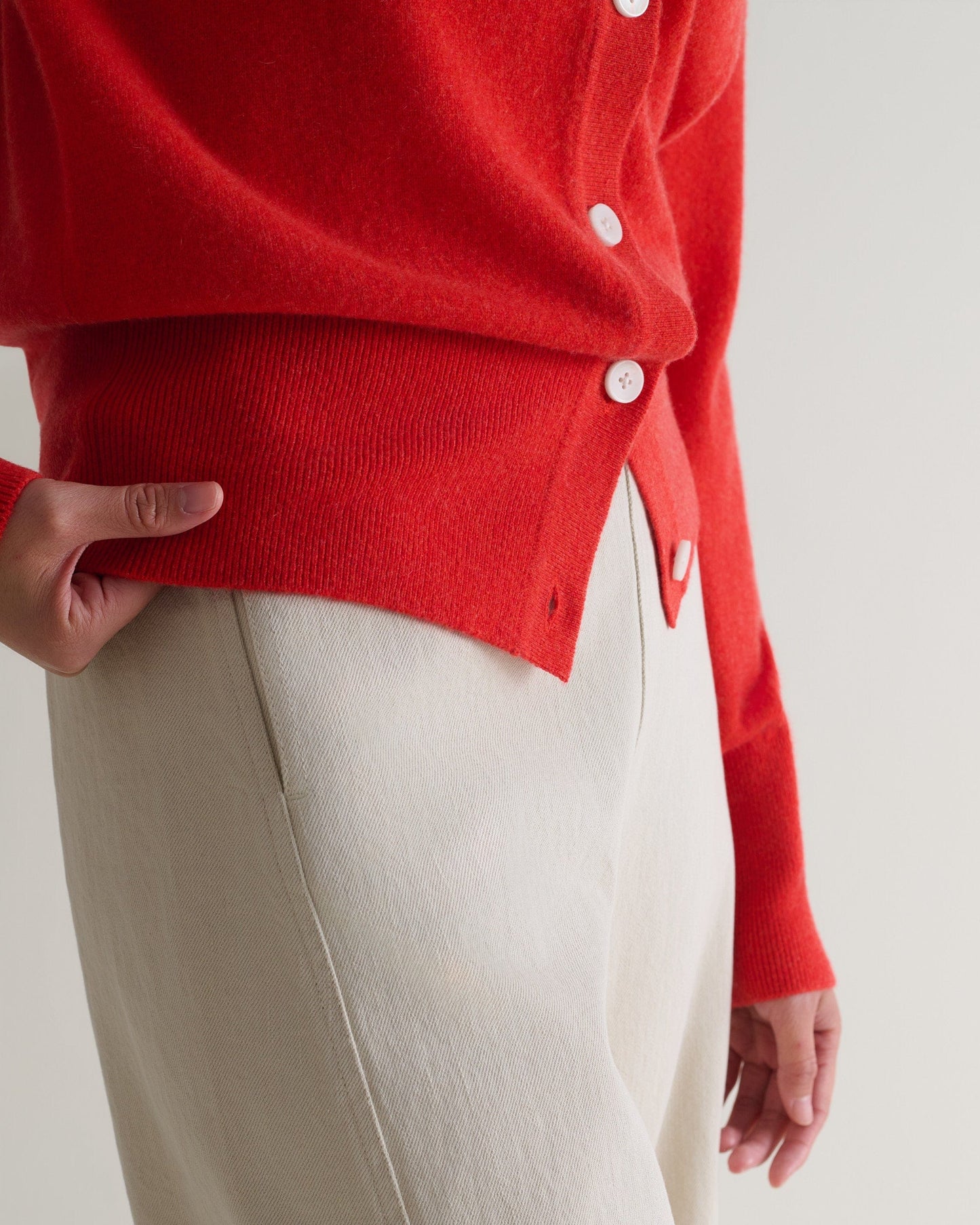 Image 5 of 5 showing a close up of Rise & Fall's poppy red fine cashmere blouson cardigan worn with cream trousers.