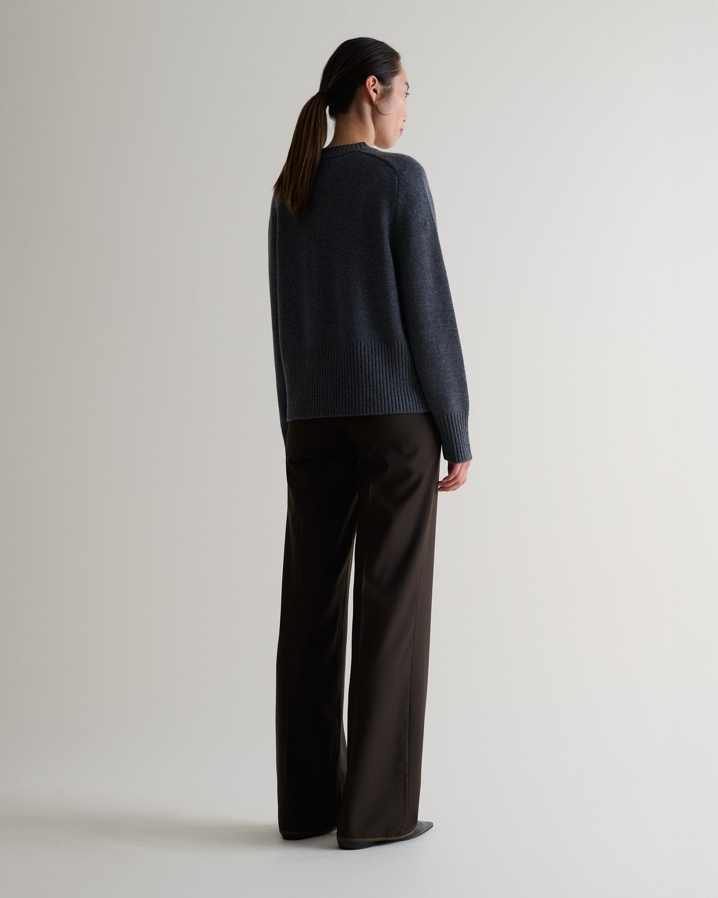 Image 5 of 5 showing back of woman wearing Rise & Fall graphite cashmere merino saddle sleeve crew neck jumper with chocolate silk trousers.