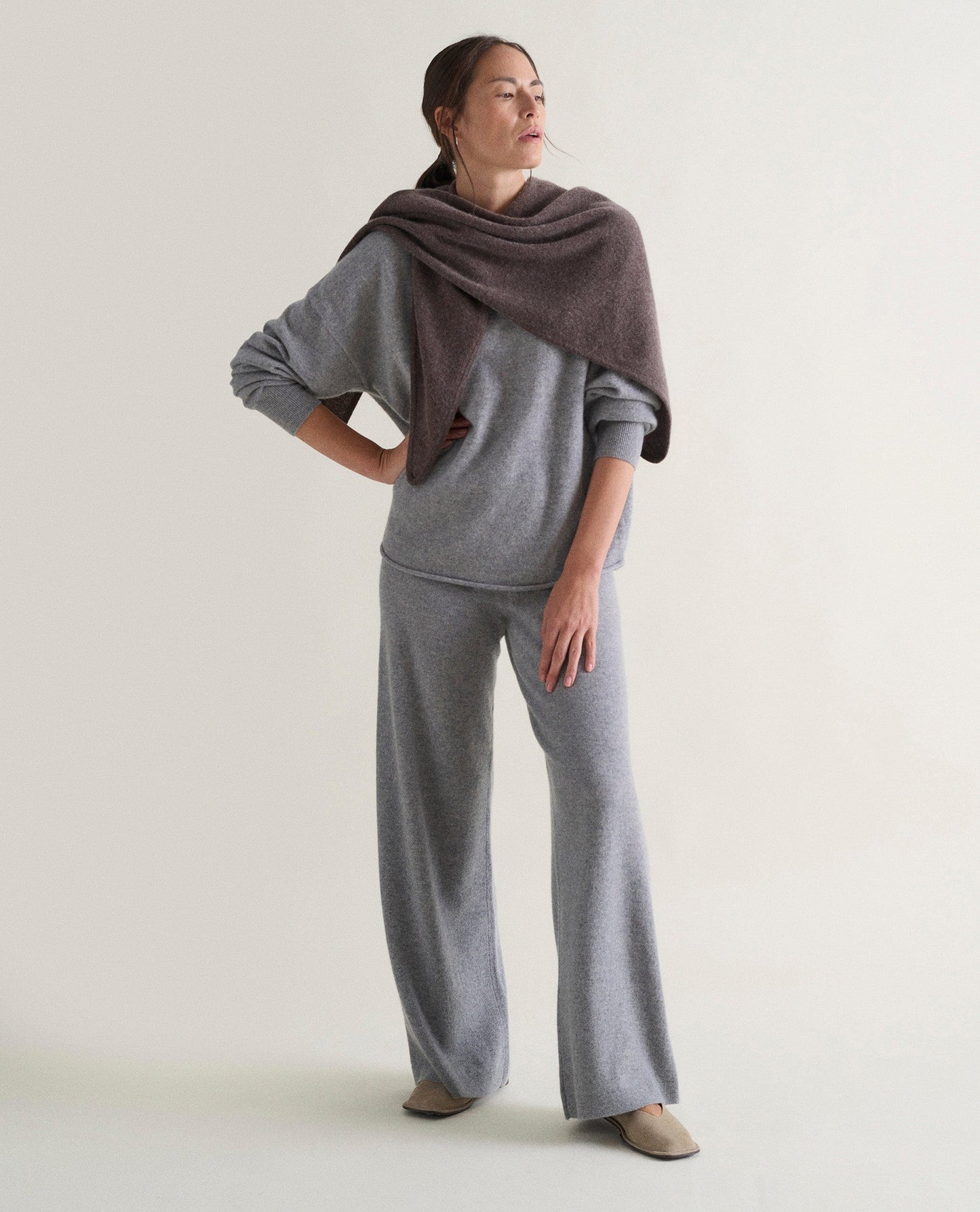 Image 5 of 5 showing woman wearing Rise & Fall's grey fine cashmere sweatshirt with matching cashmere trousers and a brown cashmere scarf.