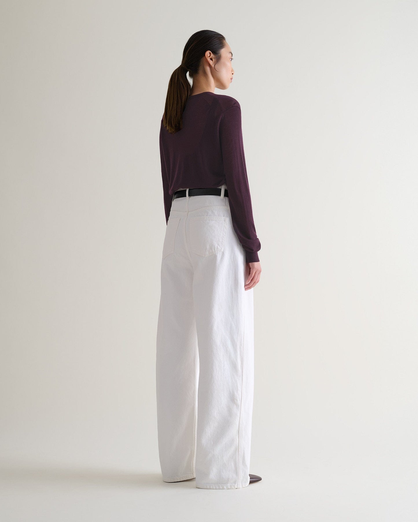 Image 5 of 5 showing back of woman wearing Rise & Fall's oxblood tencel™ cashmere double layered crew neck jumper with white jeans and black leather belt.