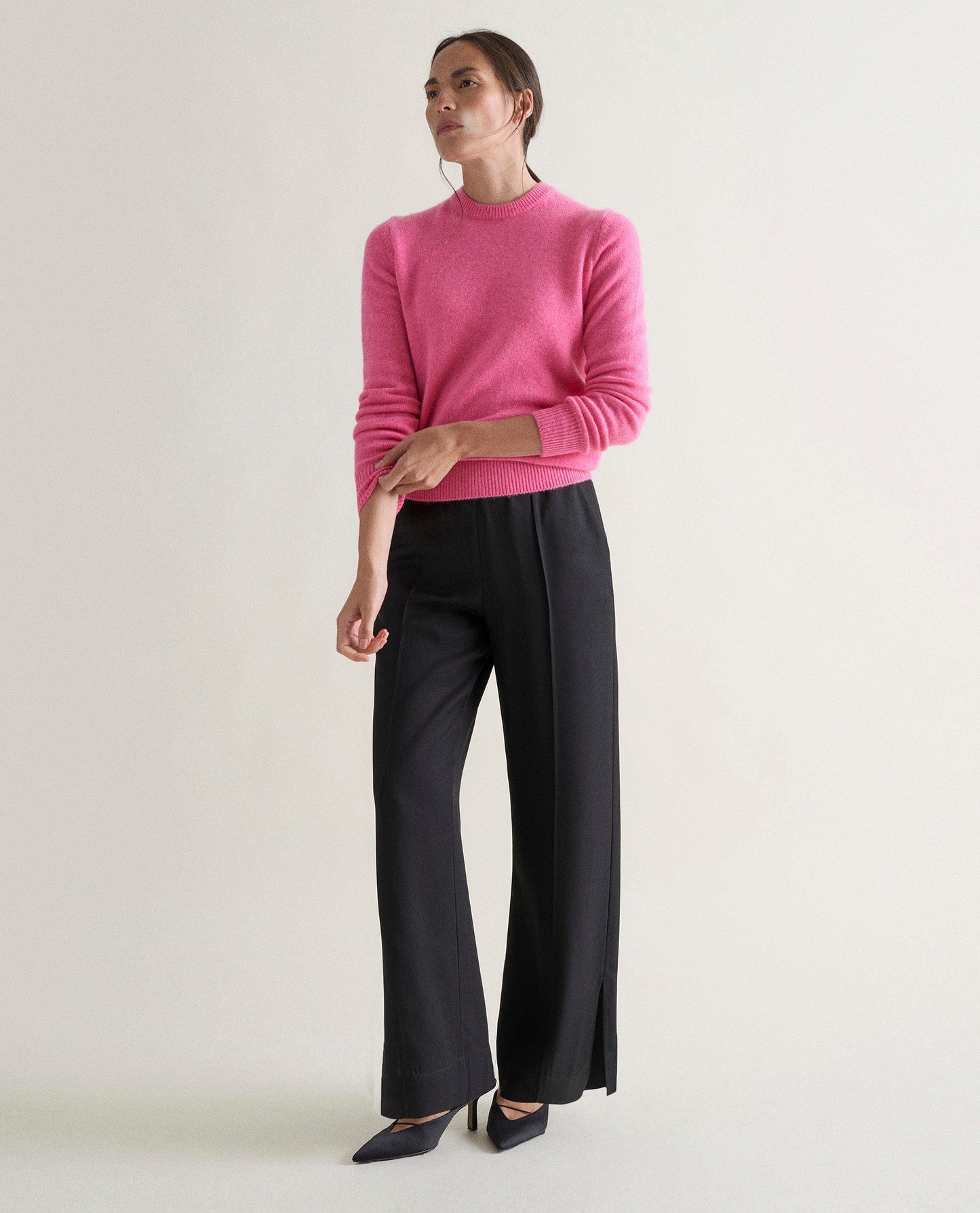 Image 5 of 5 showing woman wearing Rise & Fall's pink mid weight cashmere crew neck jumper with black trousers.