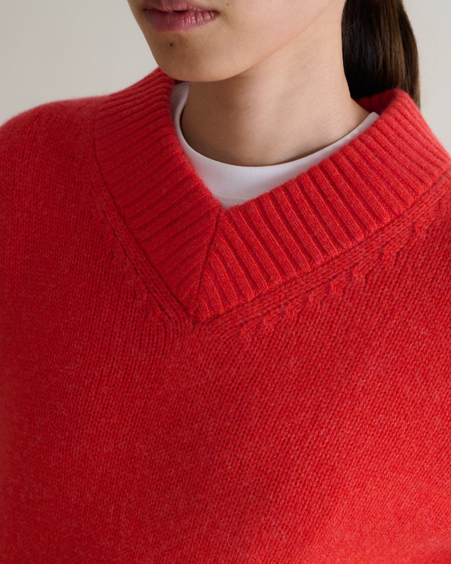 Image 5 of 6 showing close up of woman wearing Rise & Fall poppy red cashmere merino saddle sleeve crew neck jumper with white t-shirt.