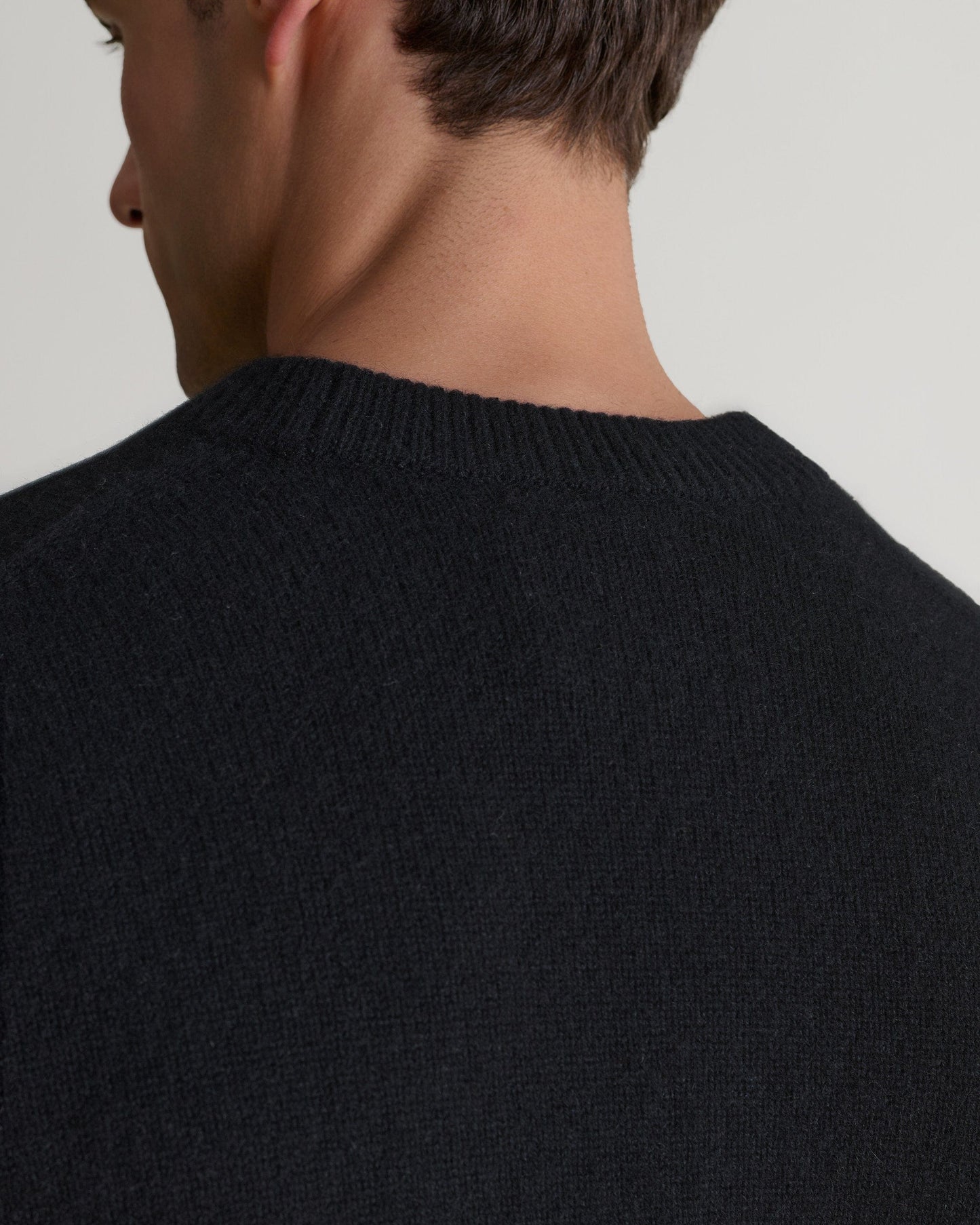 Image 5 of 7 showing close up of man wearing Rise & Fall's Finest Cashmere Mid-Weight Crew Neck Jumper in black.