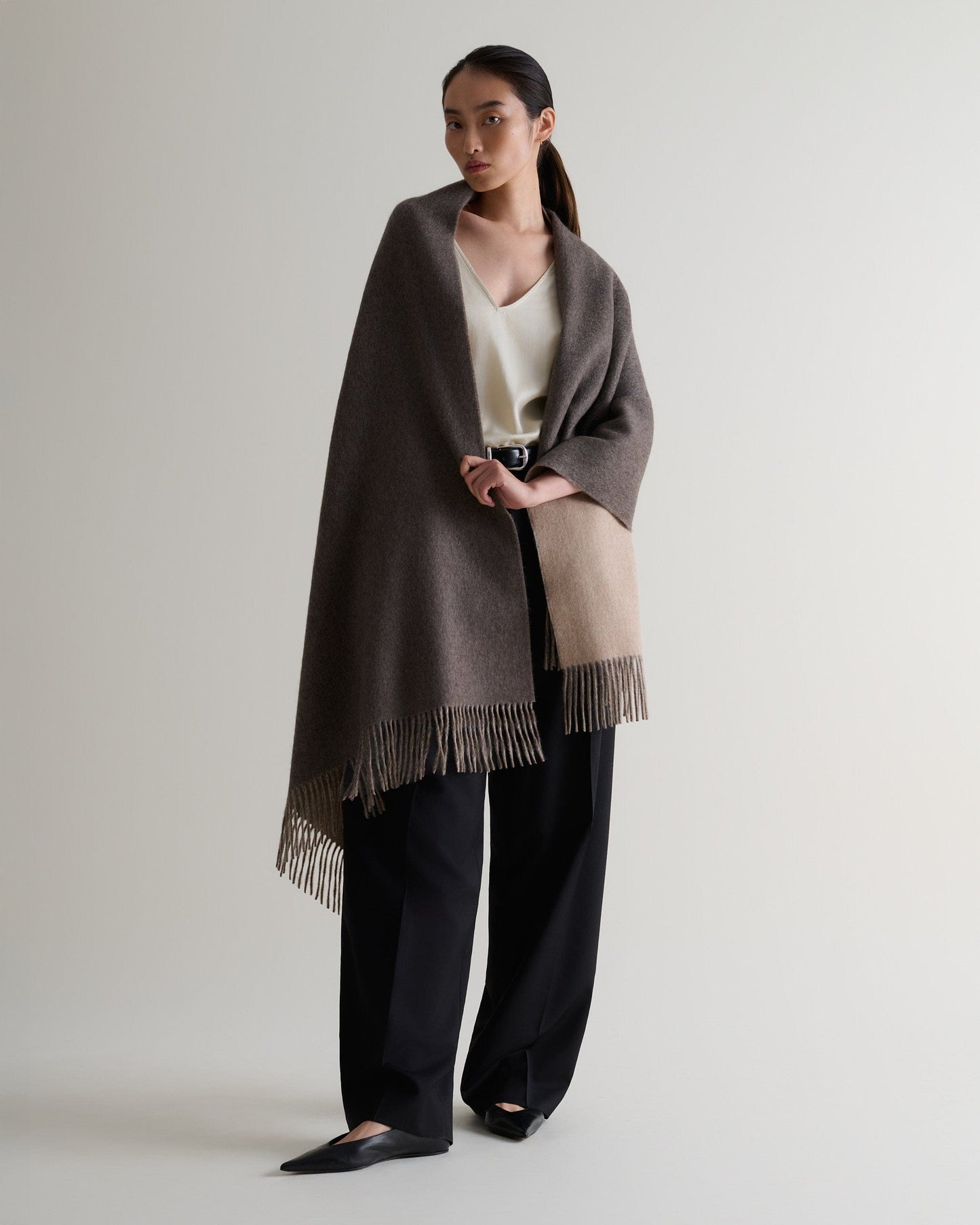 Image 5 of 7 showing woman wearing Rise & Fall's finest cashmere double faced wrap mole side with cream top and black trousers.