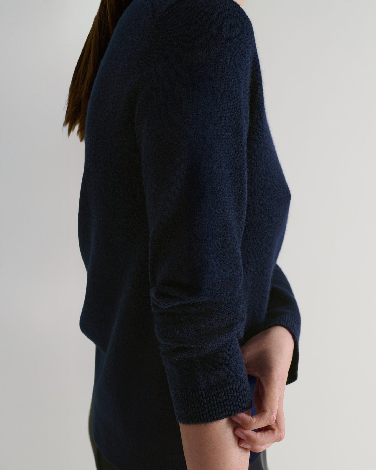 Image 6 of 6 showing side view of a woman wearing Rise & Fall's indigo cashmere merino henley jumper with black silk trousers.