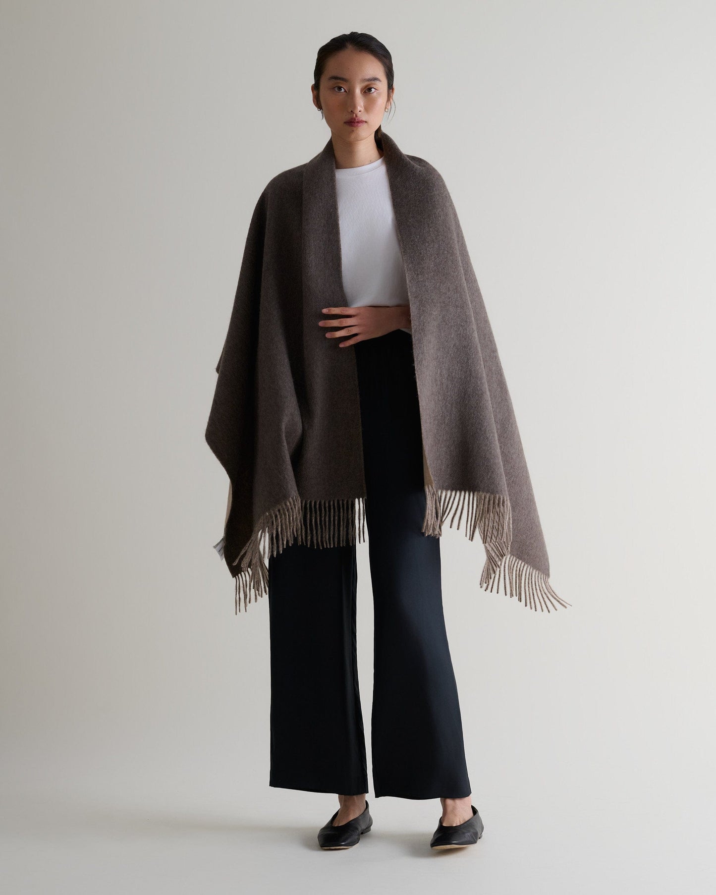 Image 6 of 7 showing woman wearing Rise & Fall's finest cashmere double faced wrap mole side with white T-shirt and black trousers.