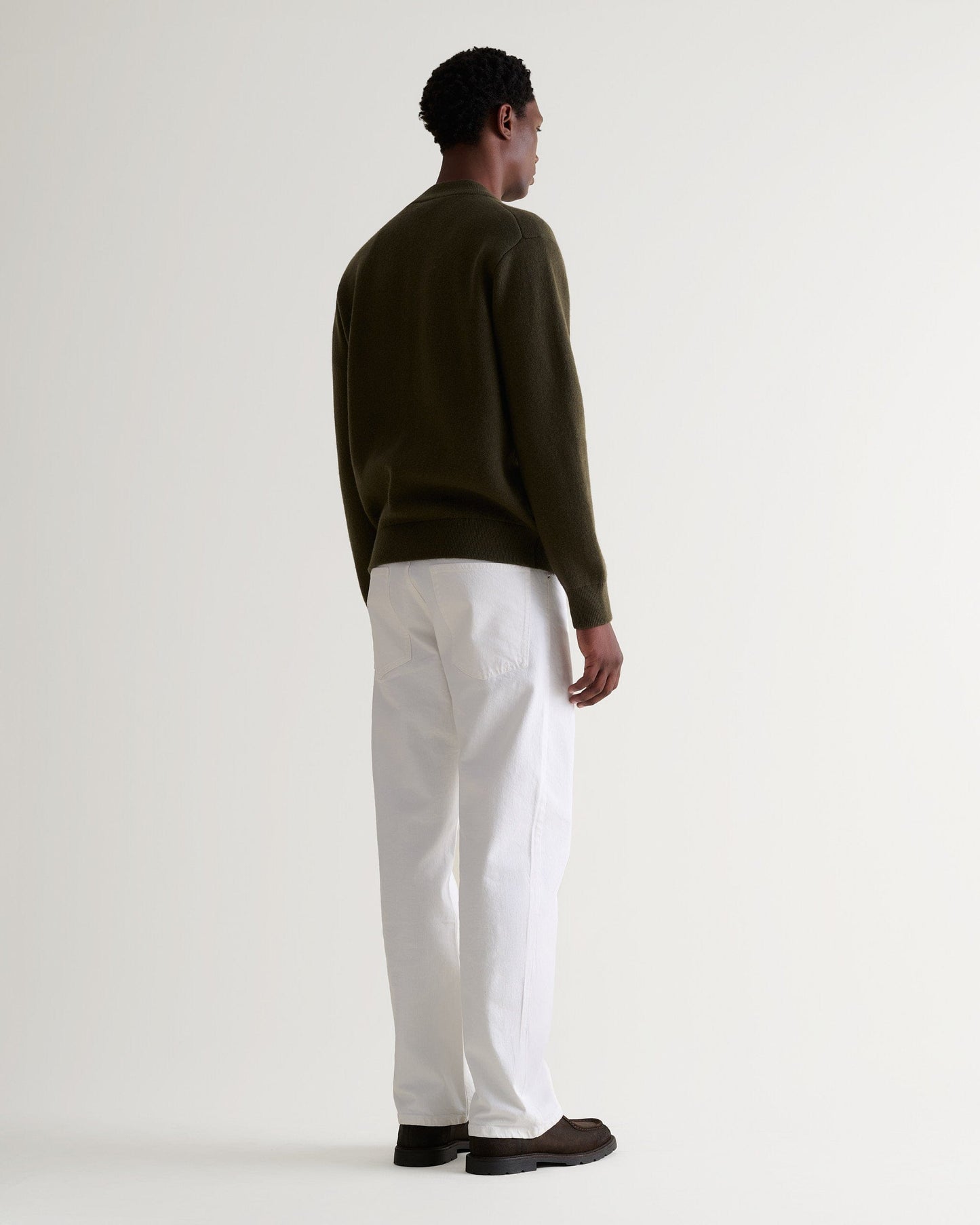 Man wears dark green cashmere merino double-faced knitted bomber with white trousers and brown shoes.