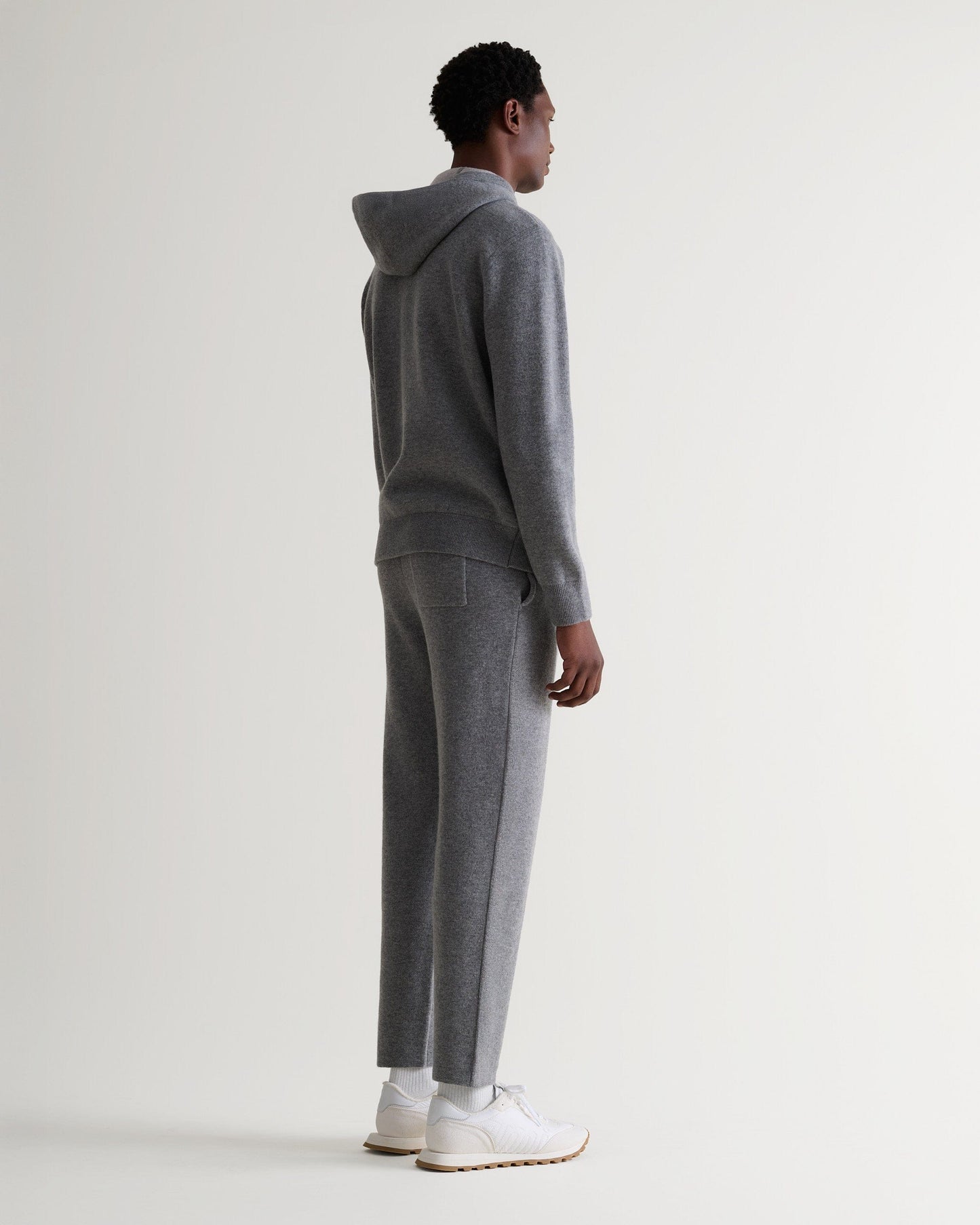 Full length side view of man wearing Rise & Fall's grey cashmere merino double-faced hoodie and matching joggers.