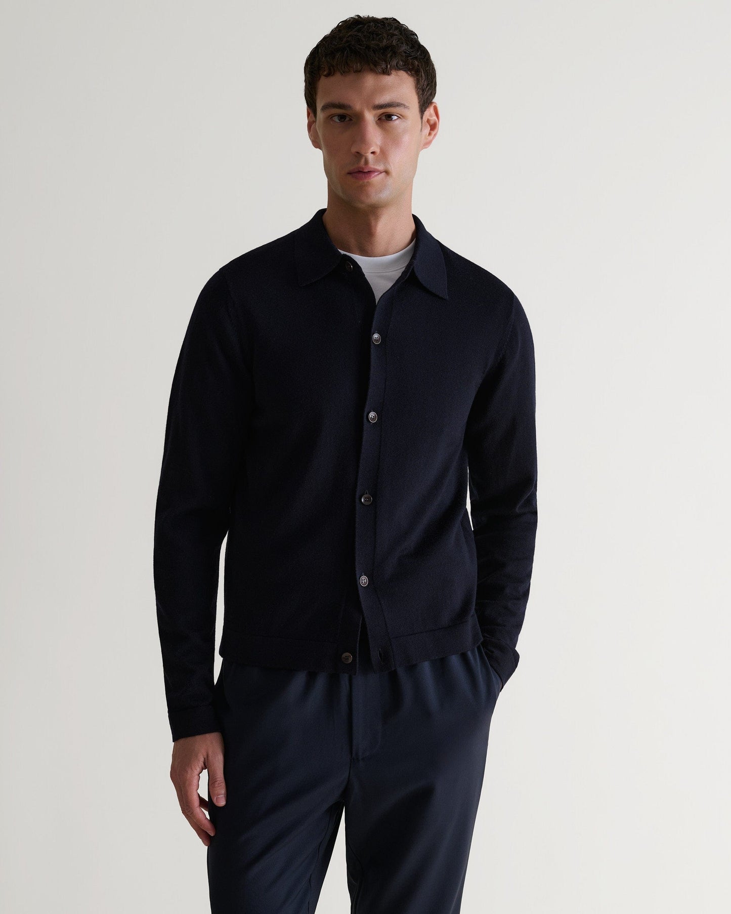 Front view of man wearing Rise & Fall's navy fine merino knit shirt. Worn with navy trousers and a white T-shirt.
