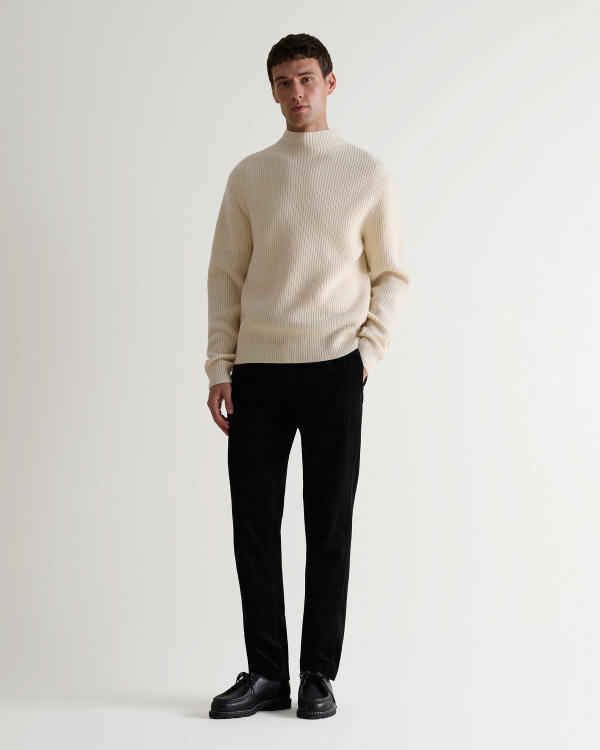 Full length front view of man wearing cream cashmere merino stand neck ribbed jumper with black trousers and leather shoes.