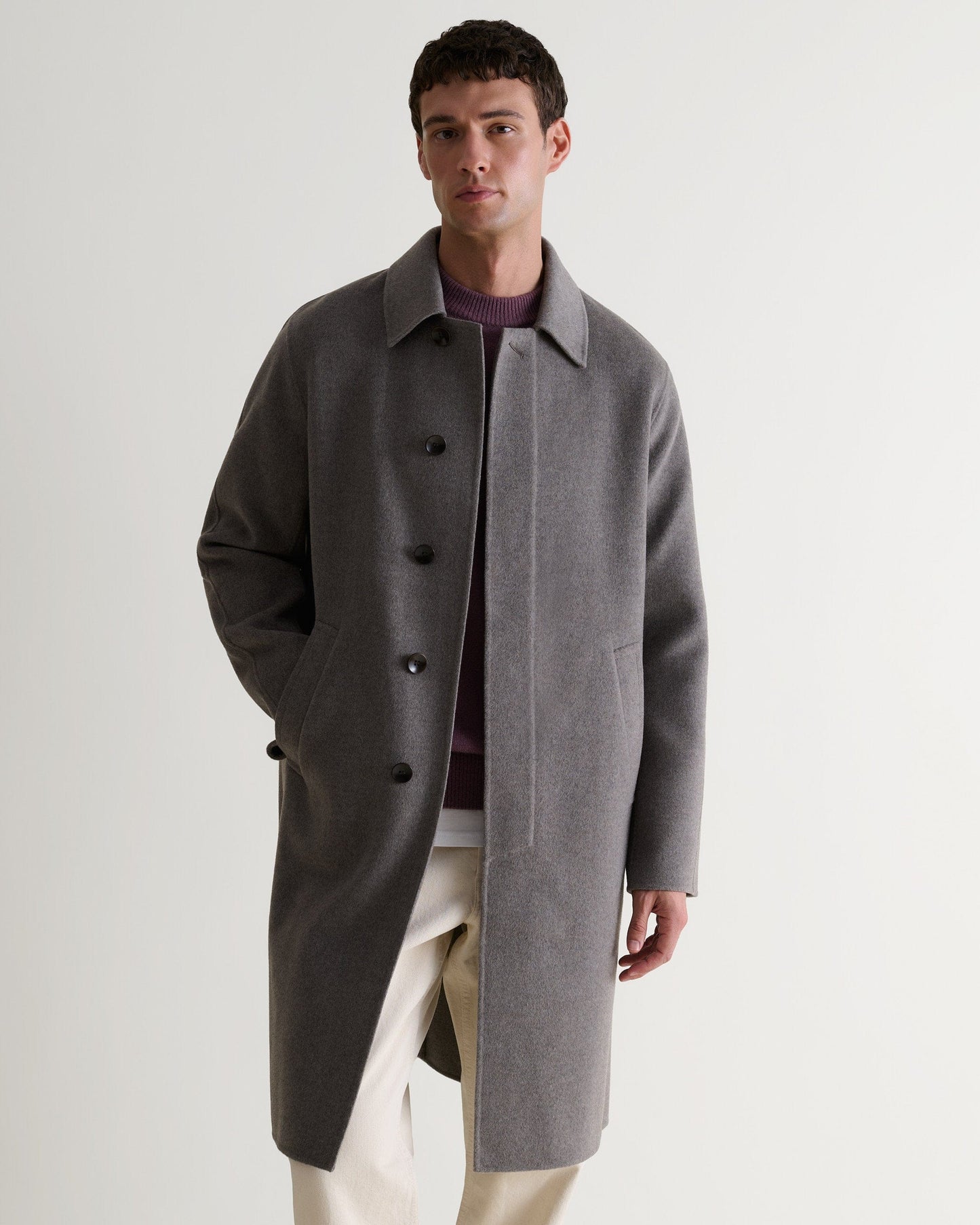 Full length view of man wearing grey cashmere merino wool double-faced coat. Paired with burgundy jumper and cream jeans.