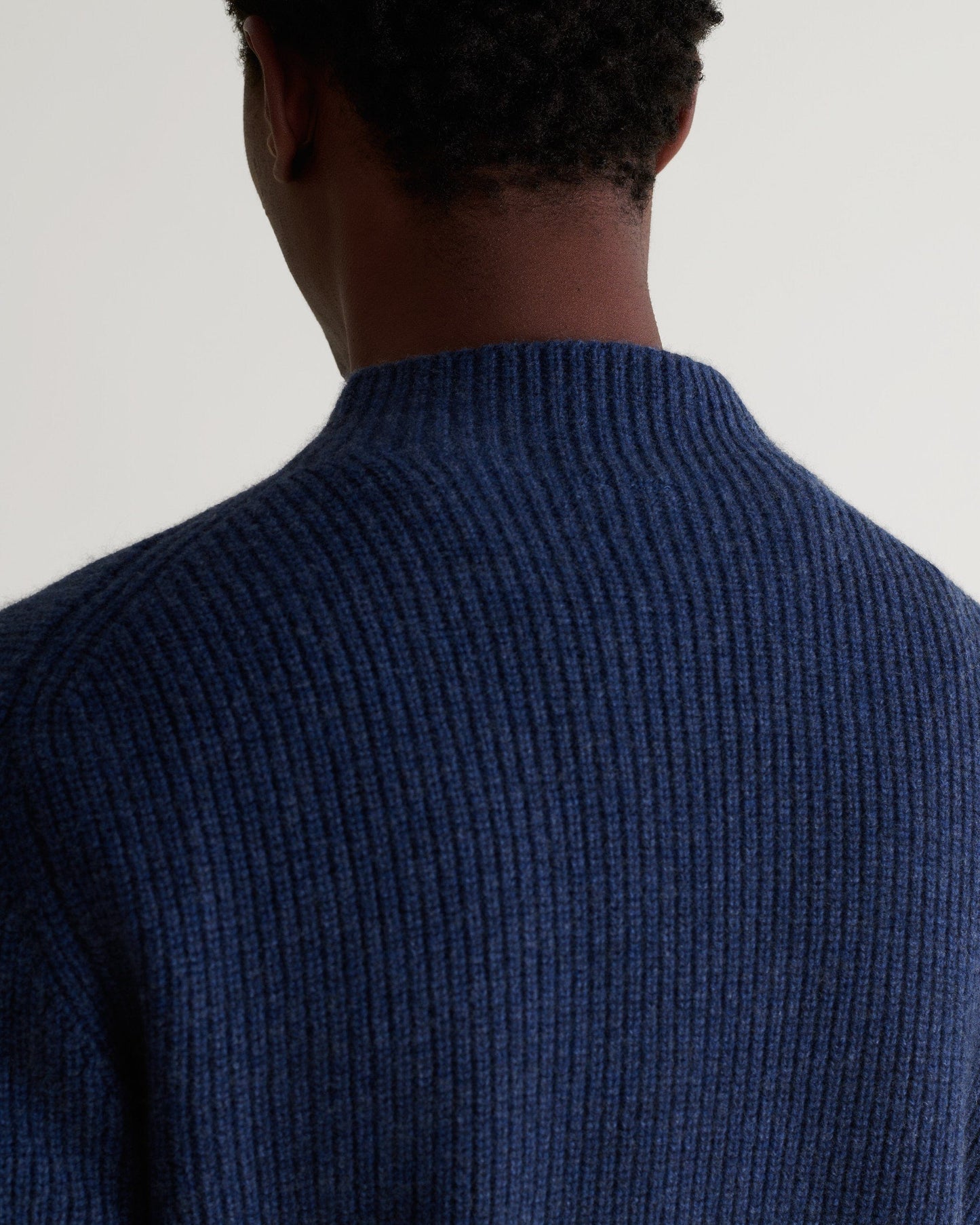 Close up back view of man wearing Rise & Fall's blue cashmere merino stand neck jumper.