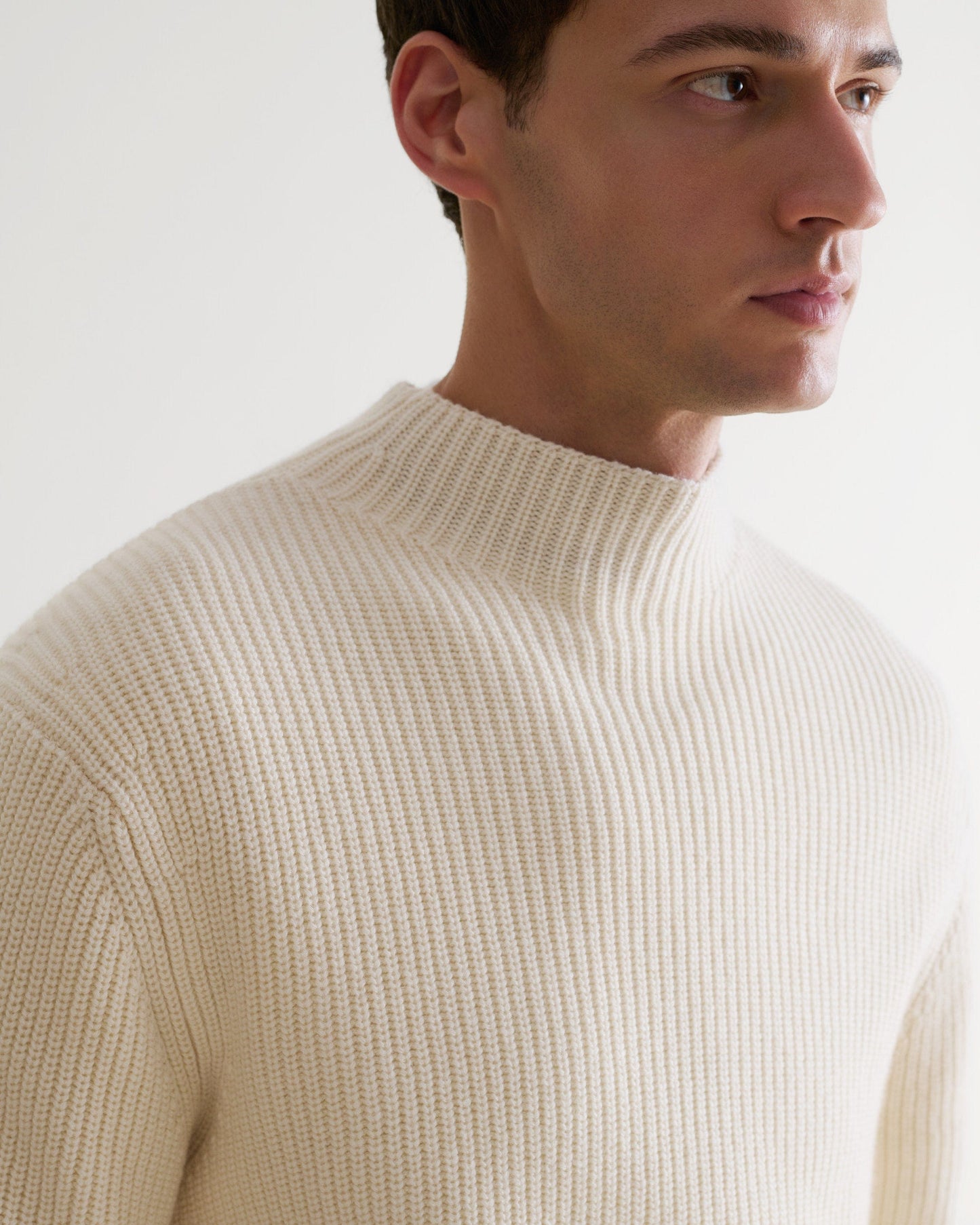 Close up side view of man wearing Rise & Fall's cream cashmere merino stand neck ribbed jumper.