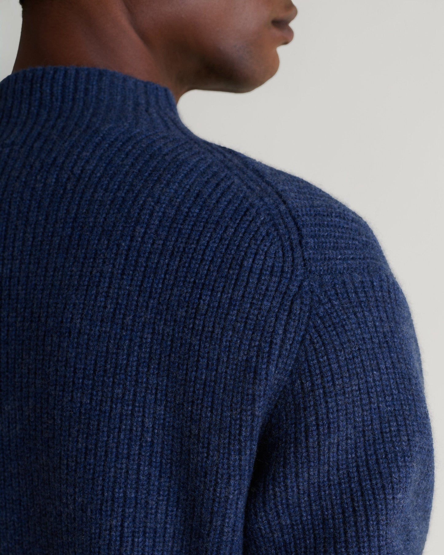 Man wears Rise & Fall's indigo blue cashmere merino stand neck jumper. A close up of shoulder.