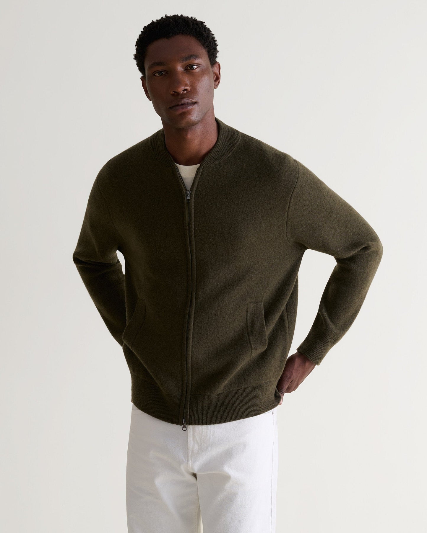Man wears Rise & Fall's military green cashmere merino double-faced knitted bomber jacket with white T-shirt and jeans.