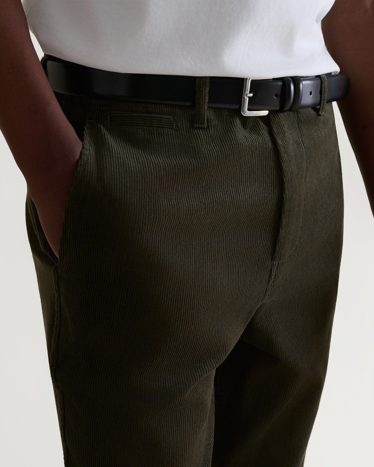 Close up front view of military green corduroy trousers being worn with white T-shirt and black leather belt.
