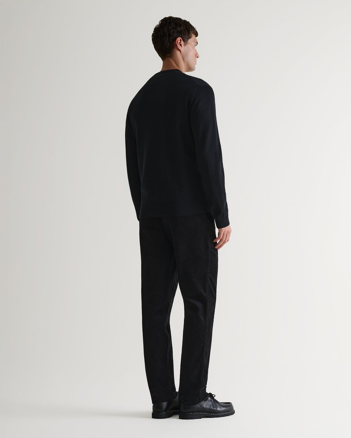 Back view of Rise & Fall's black corduroy trousers worn with black jumper and black leather shoes.