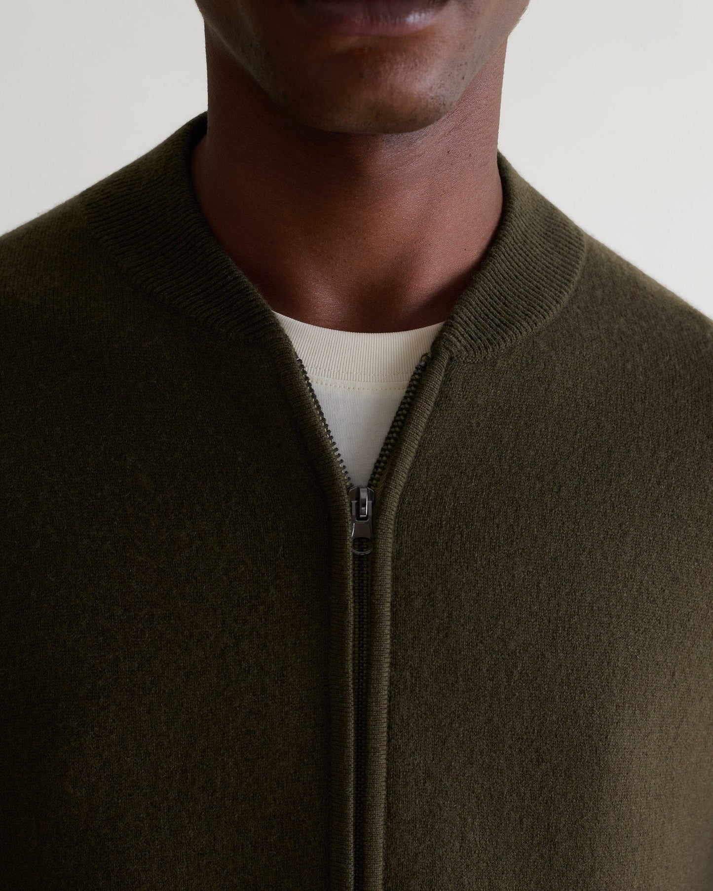 Close up neckline of Rise & Fall's dark green cashmere merino double faced zip bomber jacket with white crew neck T-shirt.