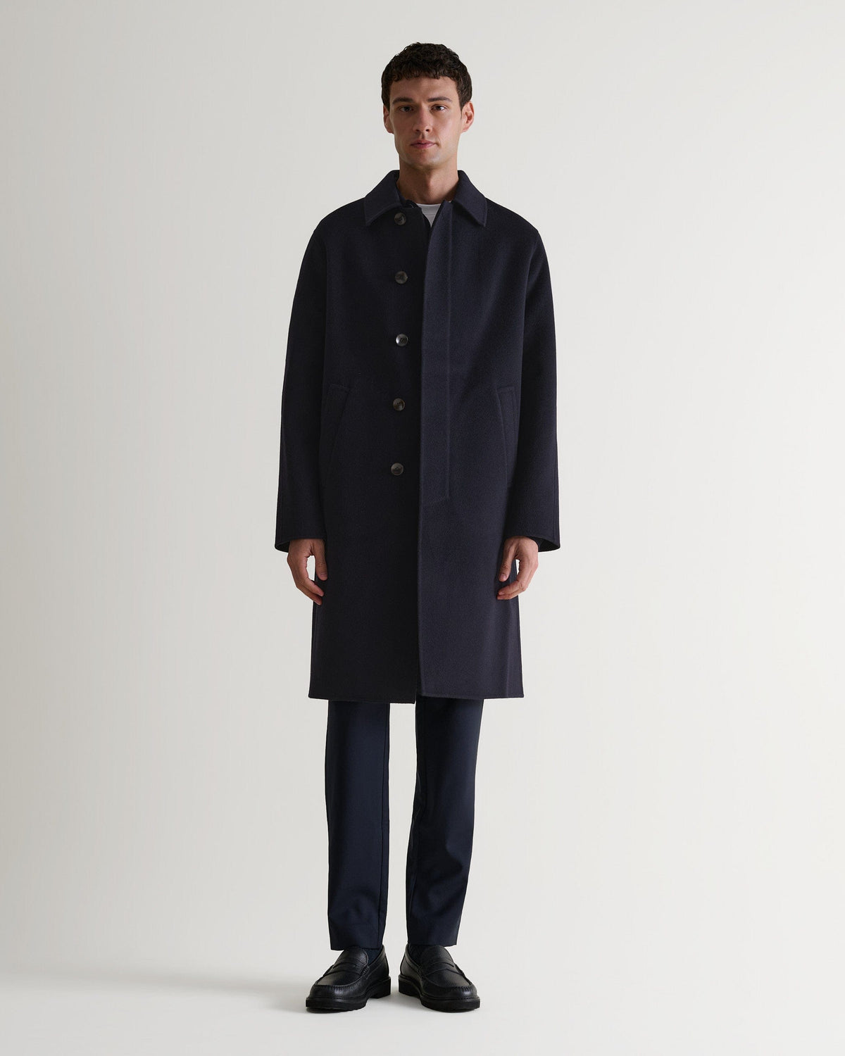 Full length front view of Rise & Fall's navy cashmere merino double-faced coat. Paired with black trousers and shoes.