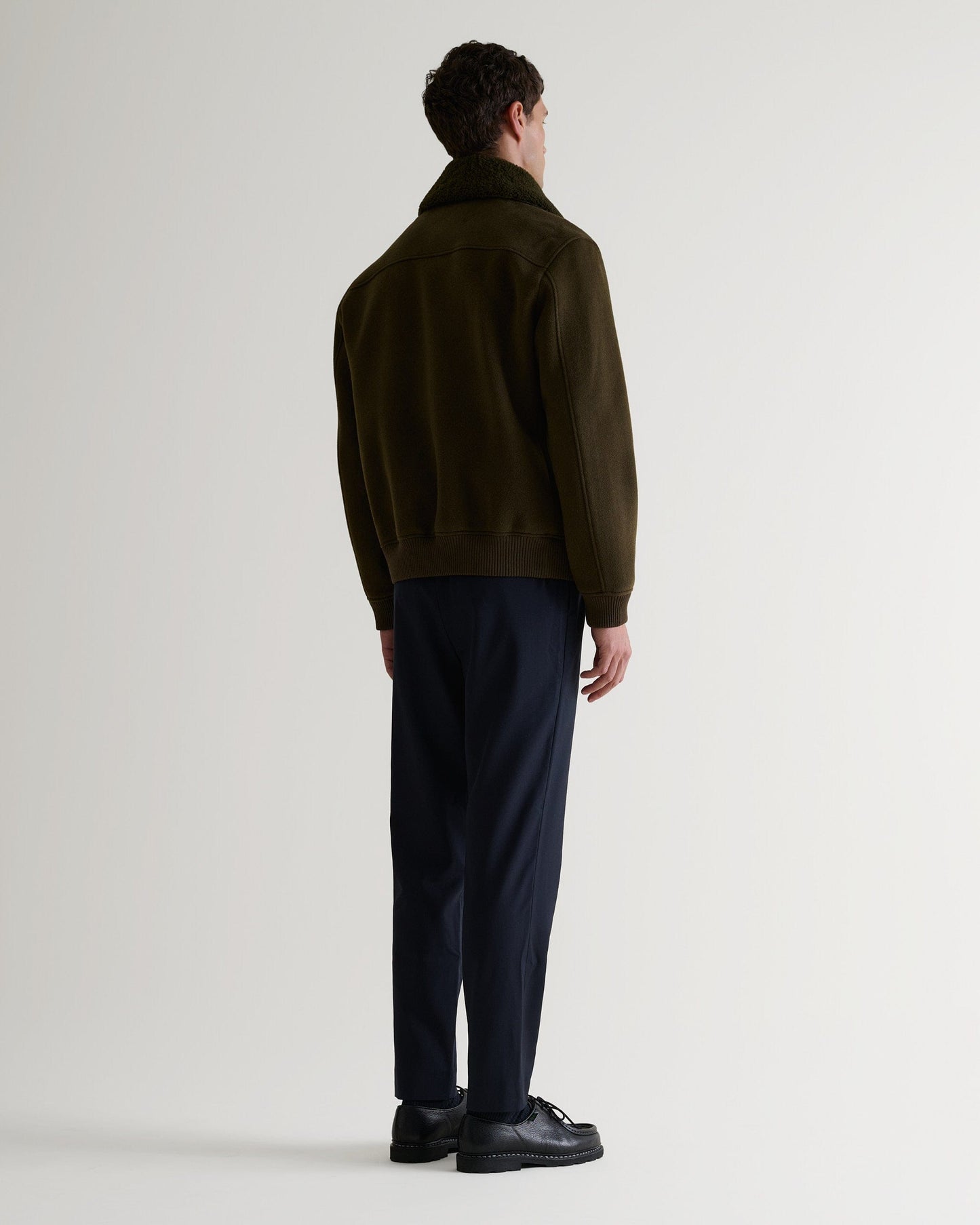 Full length back view of Rise & Fall's olive wool bomber jacket with shearling collar.