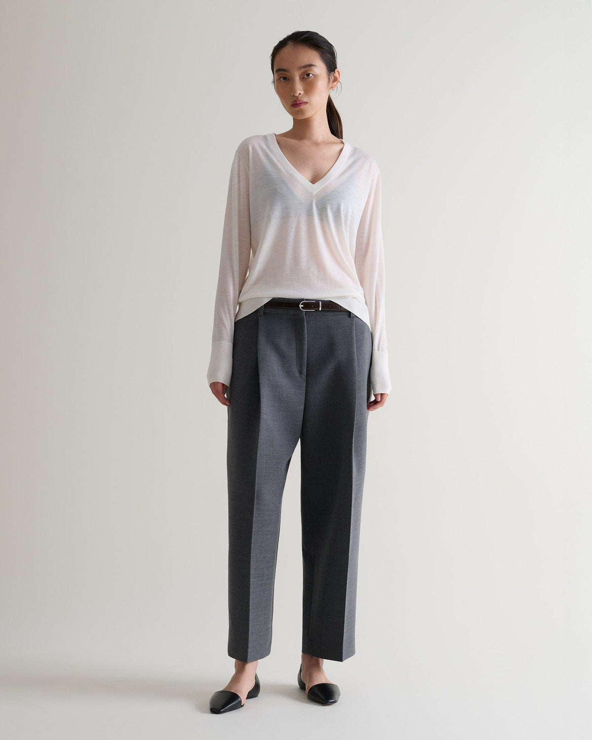 Full length front view of woman wearing Rise & Fall's cream superfine merino wool v-neck jumper.