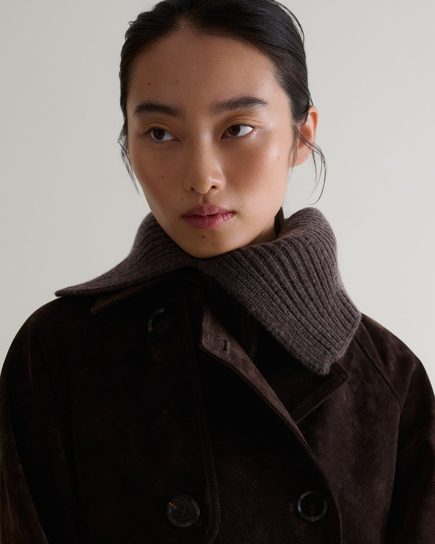 Close up of woman wearing Rise & Falls' brown cashmere merino ribbed collar. Worn with chocolate suede trench coat.