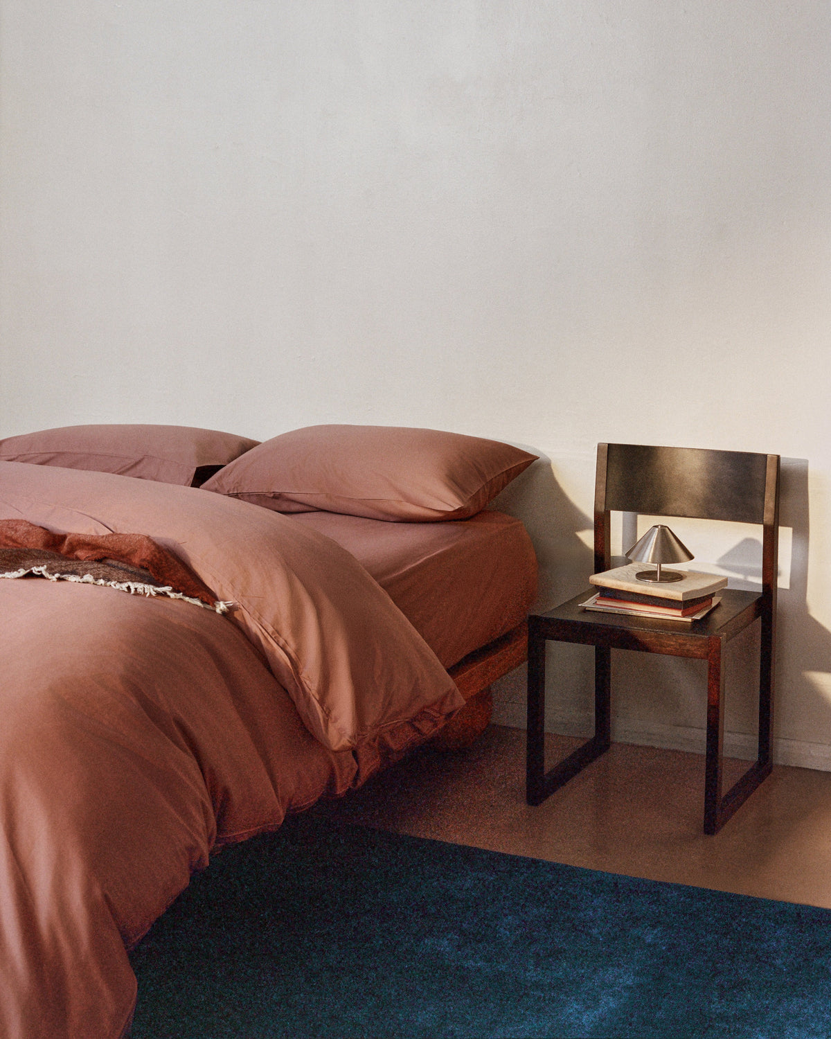 A bed made with cotton bed linen in clay during sunset.