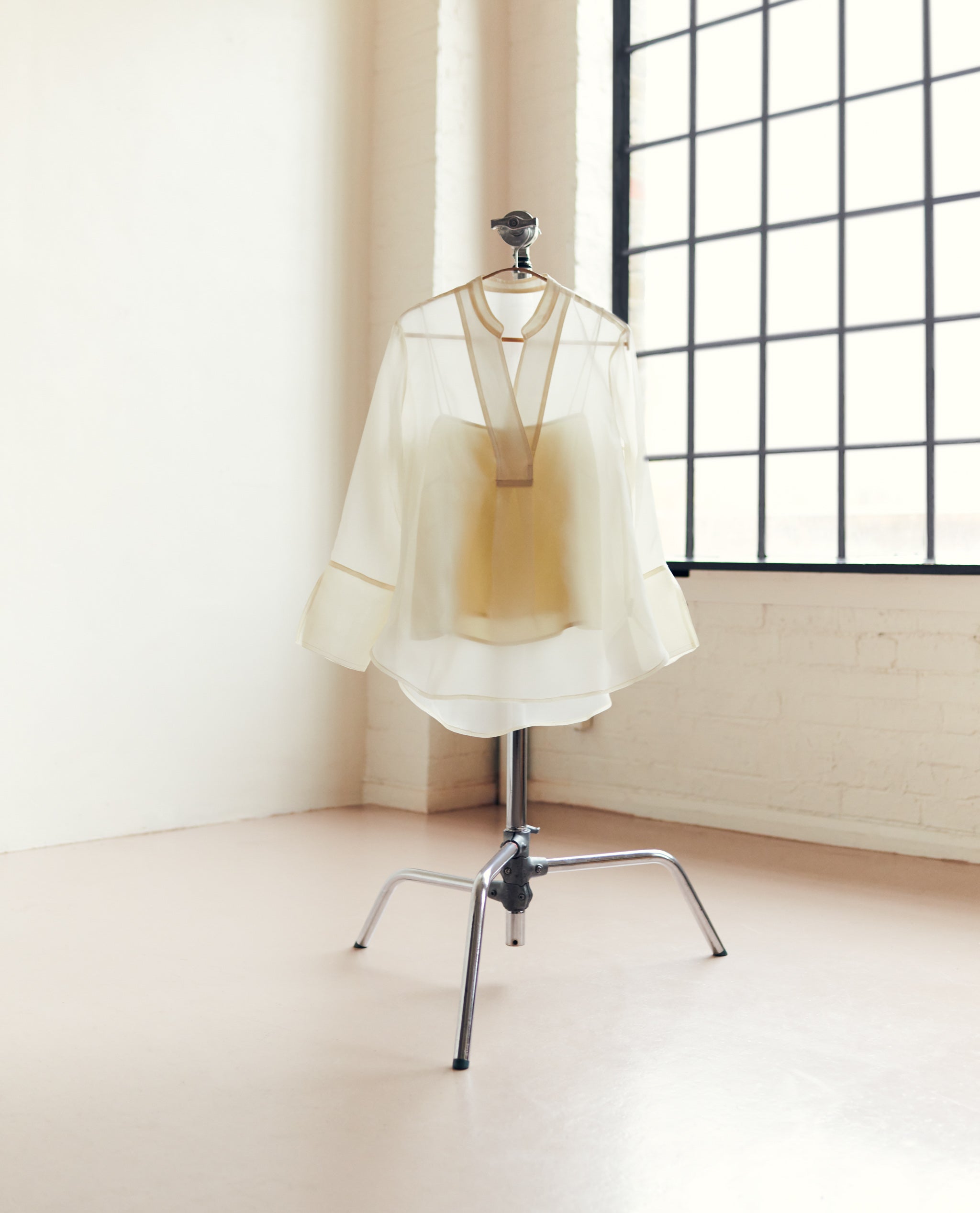 cream silk orgaza blouse on a metal stand.