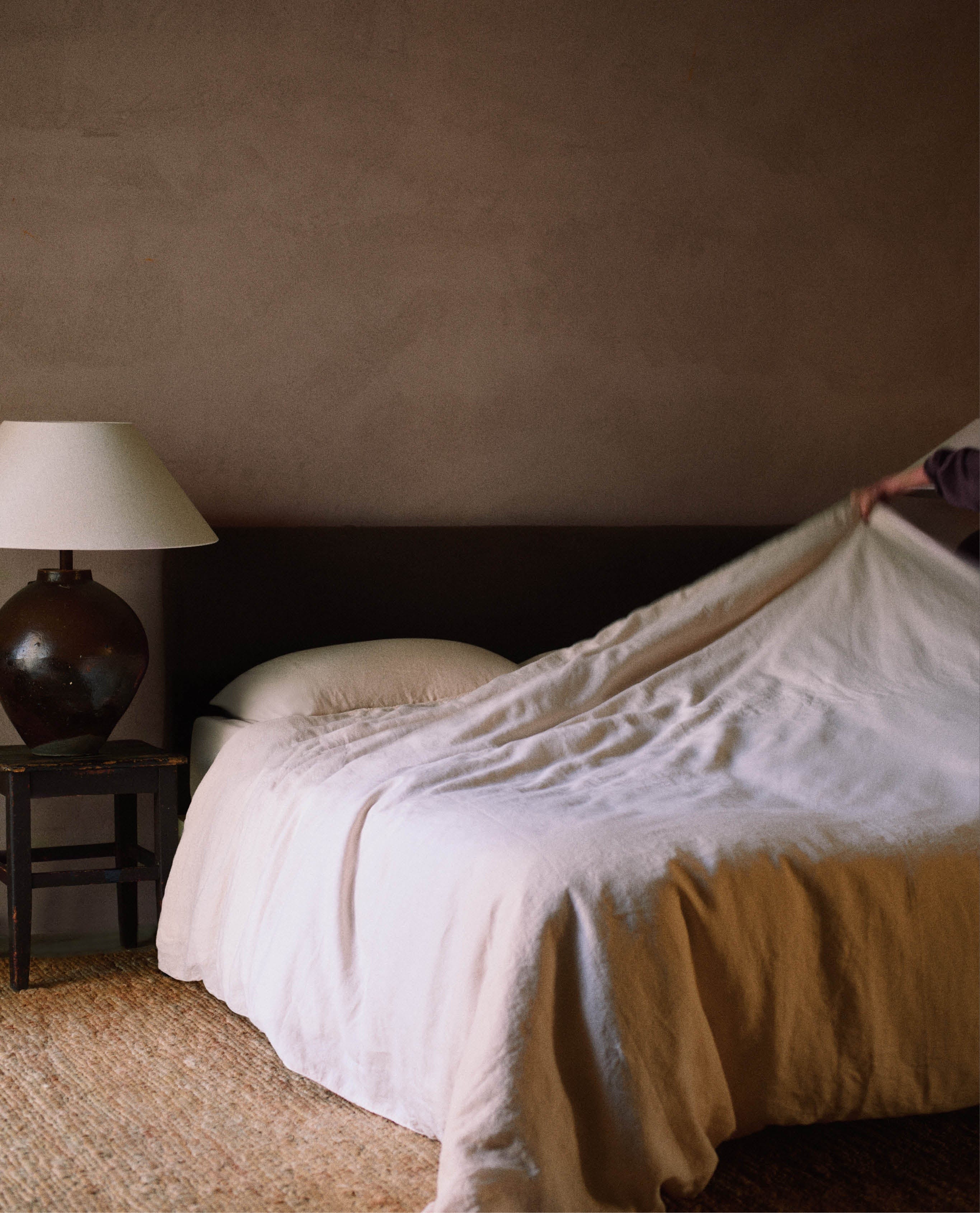 Light peach linen bedding being pulled onto a bed.