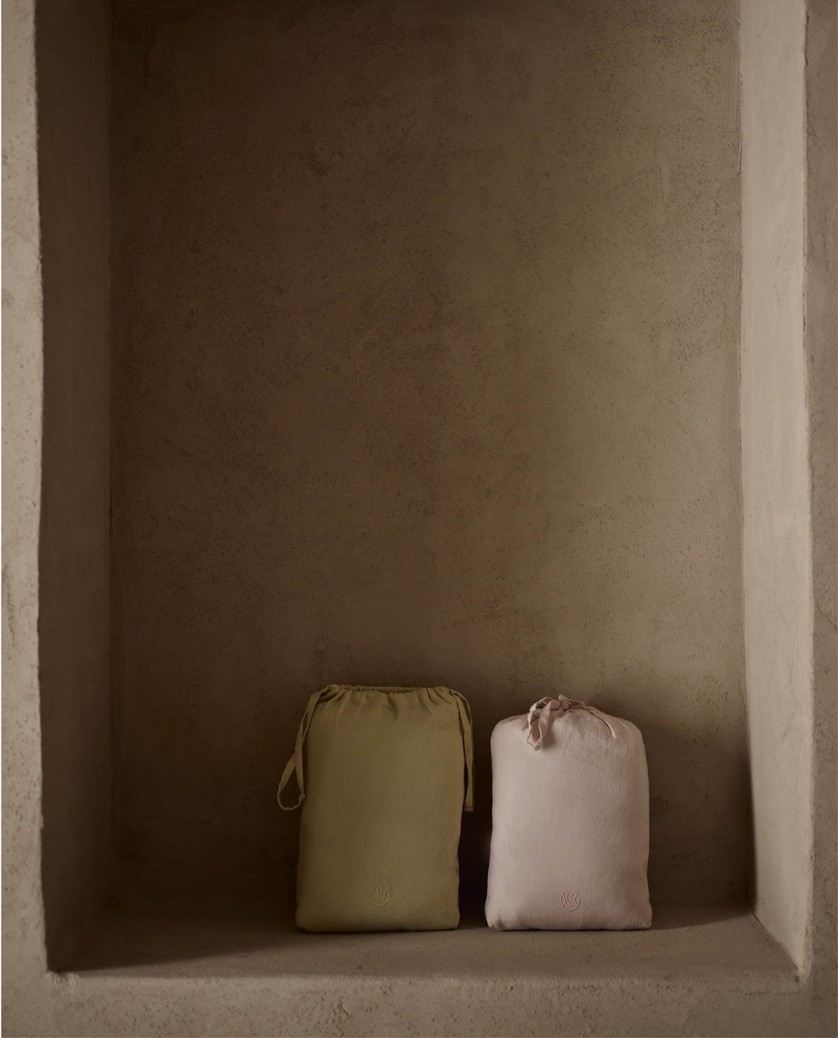 Two sets of linen bed sheets in linen bags, resting against a wall.