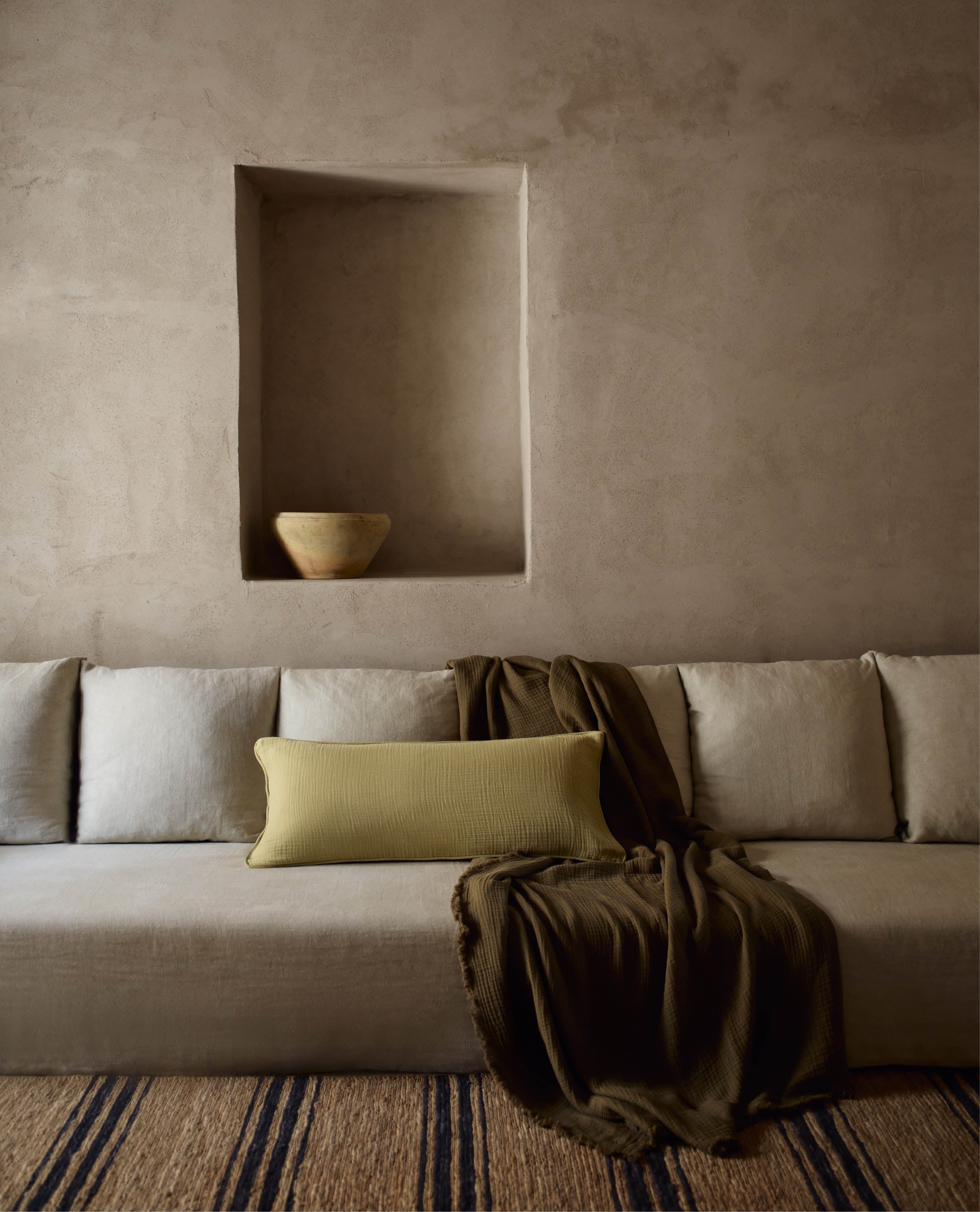 A brown velvet cotton throw with a light green cotton muslin lumbar cushion placed on a long beige sofa